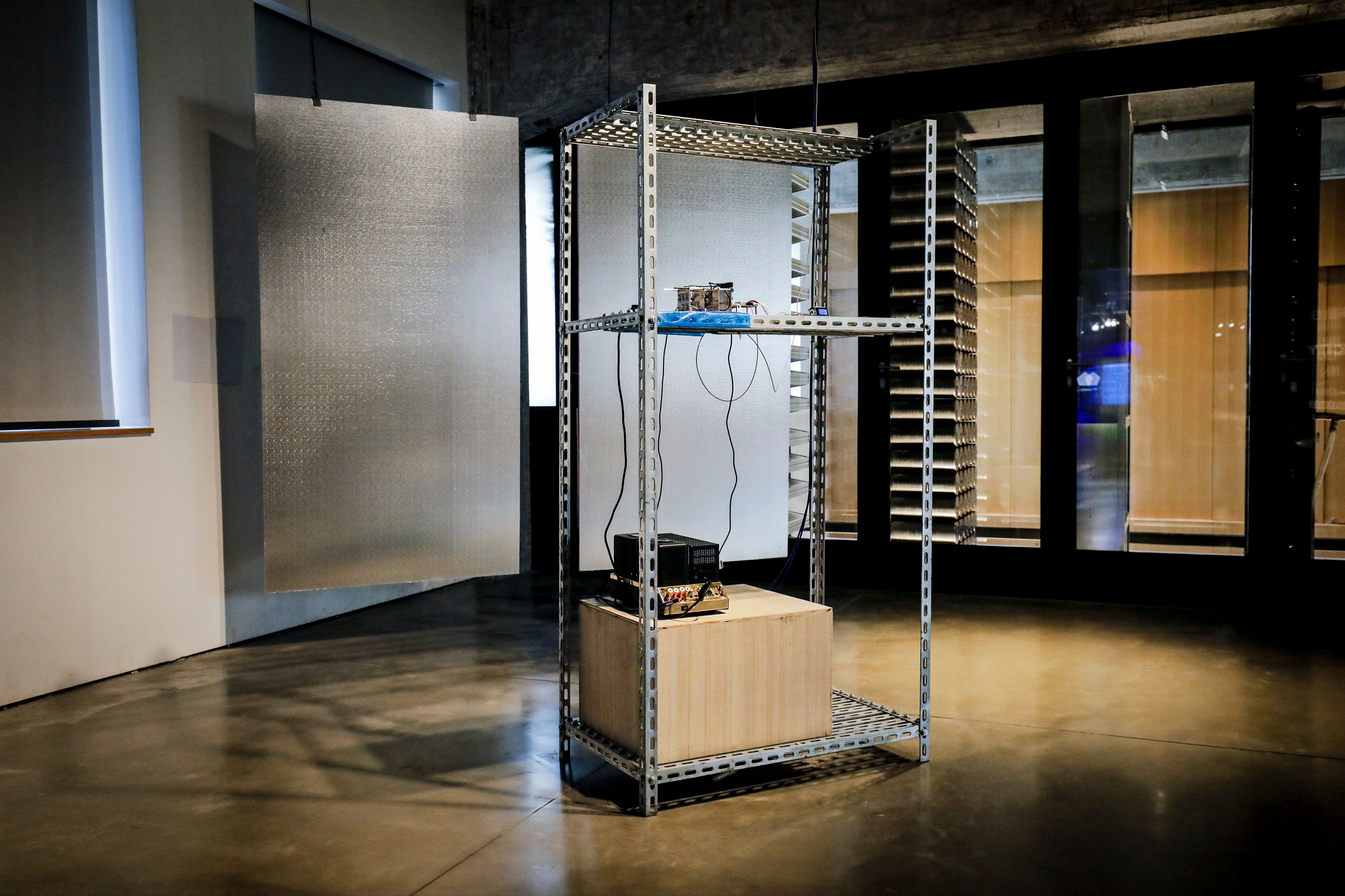Metal shelving unit with electronic equipment in an art installation.