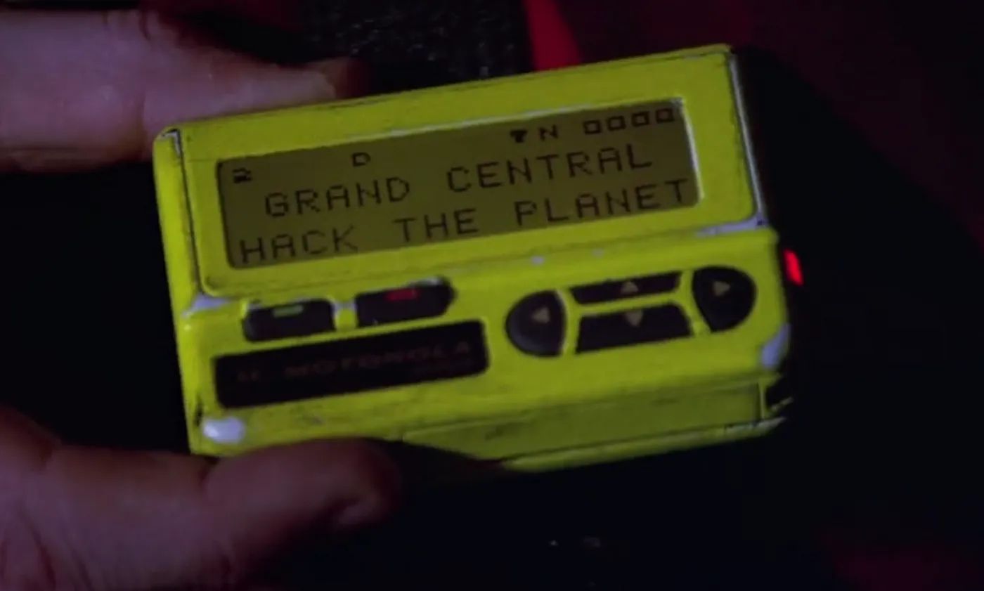 Close-up of a yellow pager displaying the message "GRAND CENTRAL HACK THE PLANET."