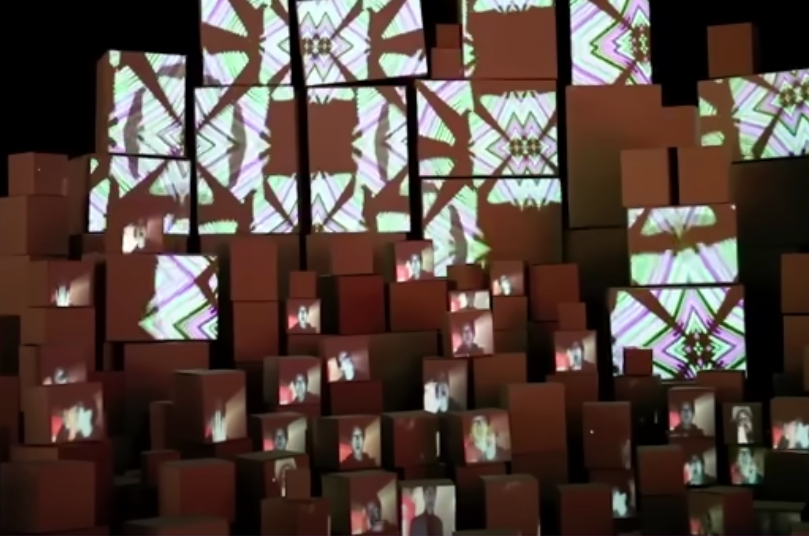 Multiple human figures and abstract art projections illuminate a room filled with scattered boxes.