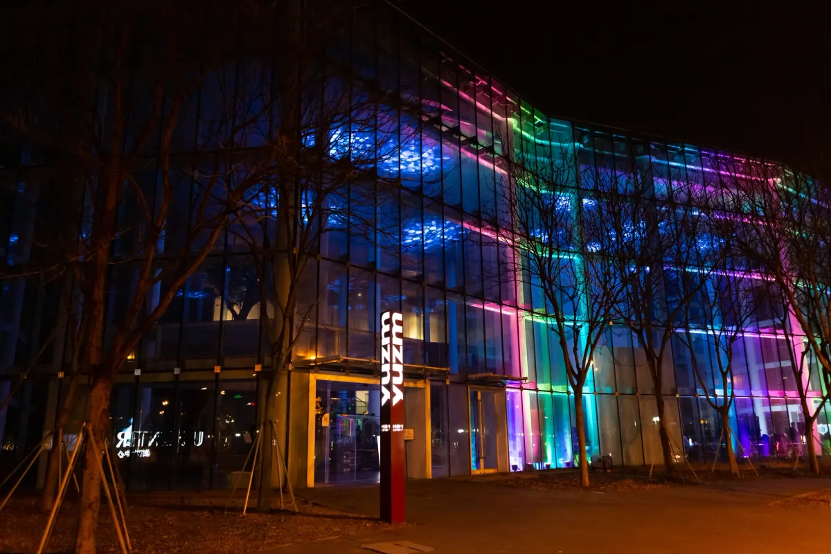 An illuminated building at night with multiple windows, adorned with an array of colorful lights on its façade.