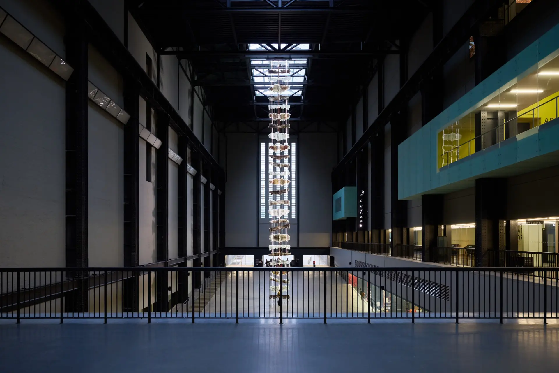 A wide view of a vast industrial hall shows the towering hanging installation of animal hides extending from ceiling to floor.
