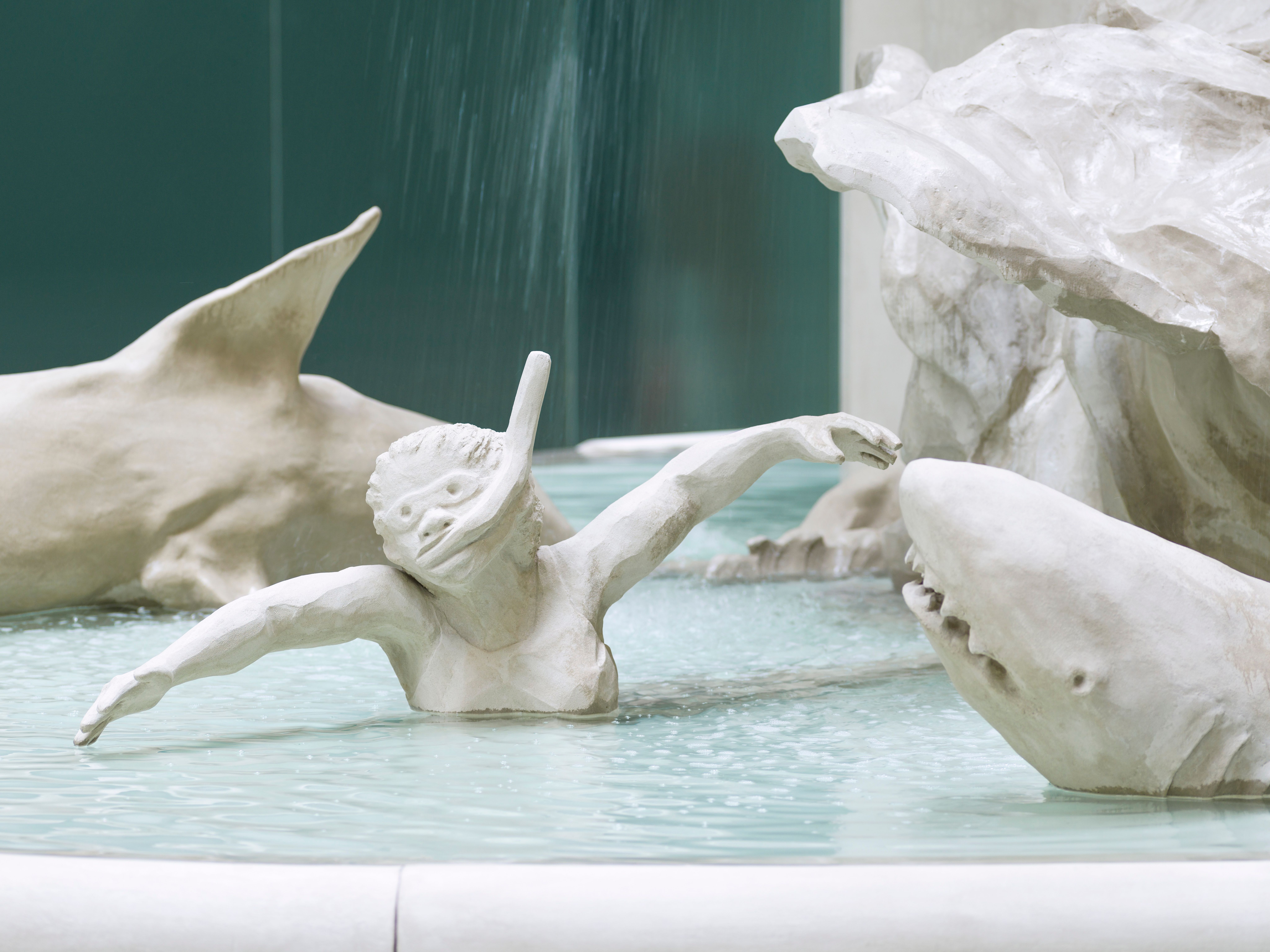 Detail of an artistic, white fountain with focus on a statue of a diver encircled by sharks, part of Kara Walker's "Fons A...