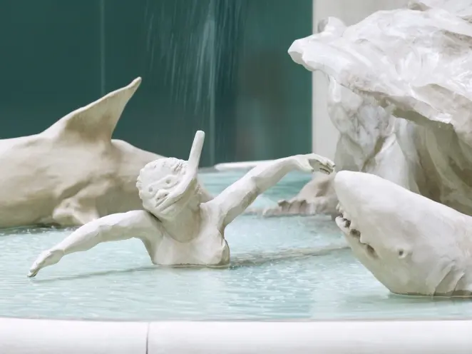 Detail of an artistic, white fountain with focus on a statue of a diver encircled by sharks, part of Kara Walker's "Fons A...