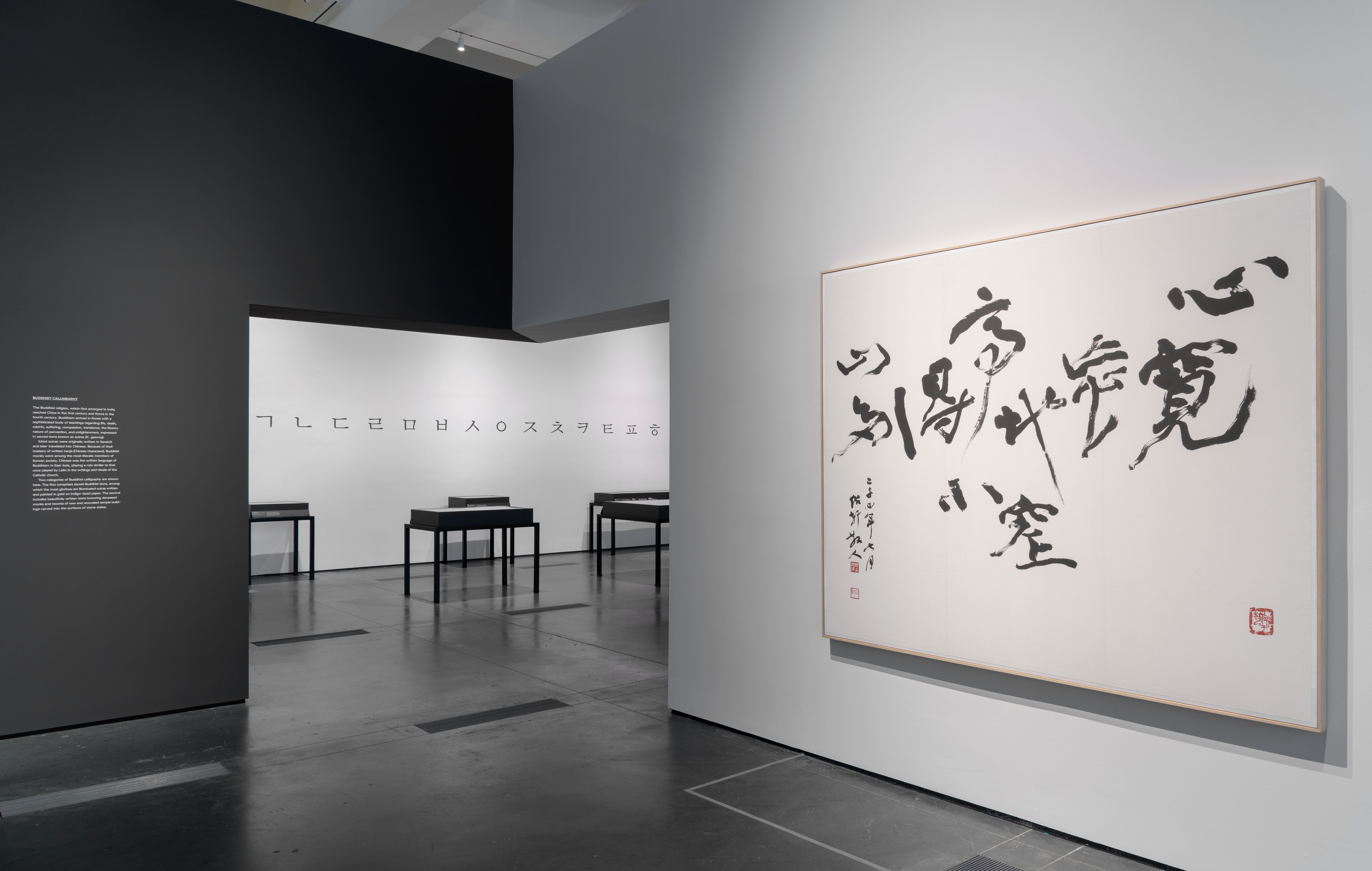 A dark-floored gallery room at the Los Angeles County Museum of Art, adorned with various framed art pieces hanging on the...
