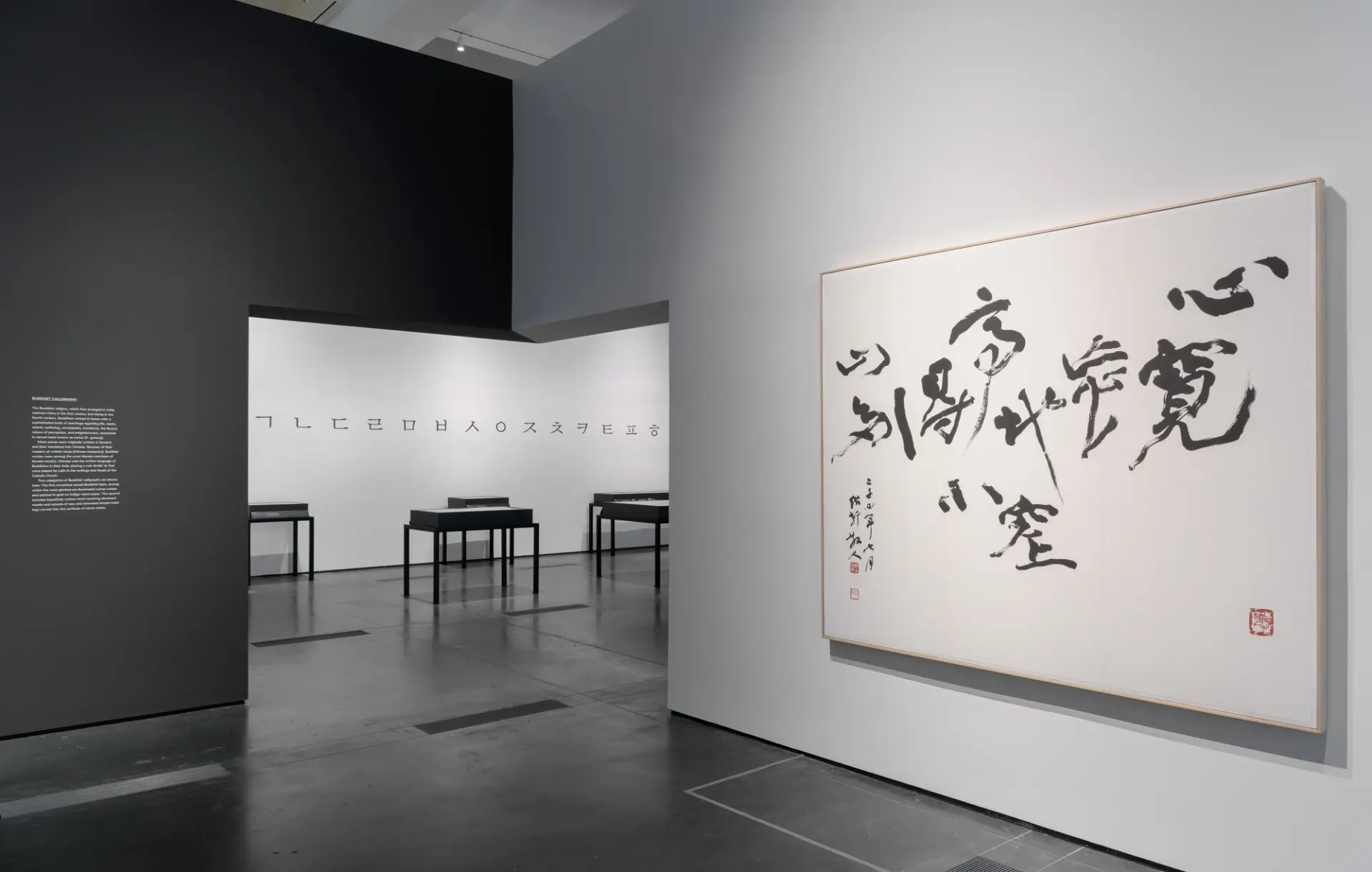 A dark-floored gallery room at the Los Angeles County Museum of Art, adorned with various framed art pieces hanging on the...