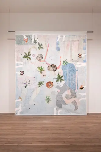 An abstract tapestry artwork featuring human and plant forms, suspended in a gallery with a wooden floor.