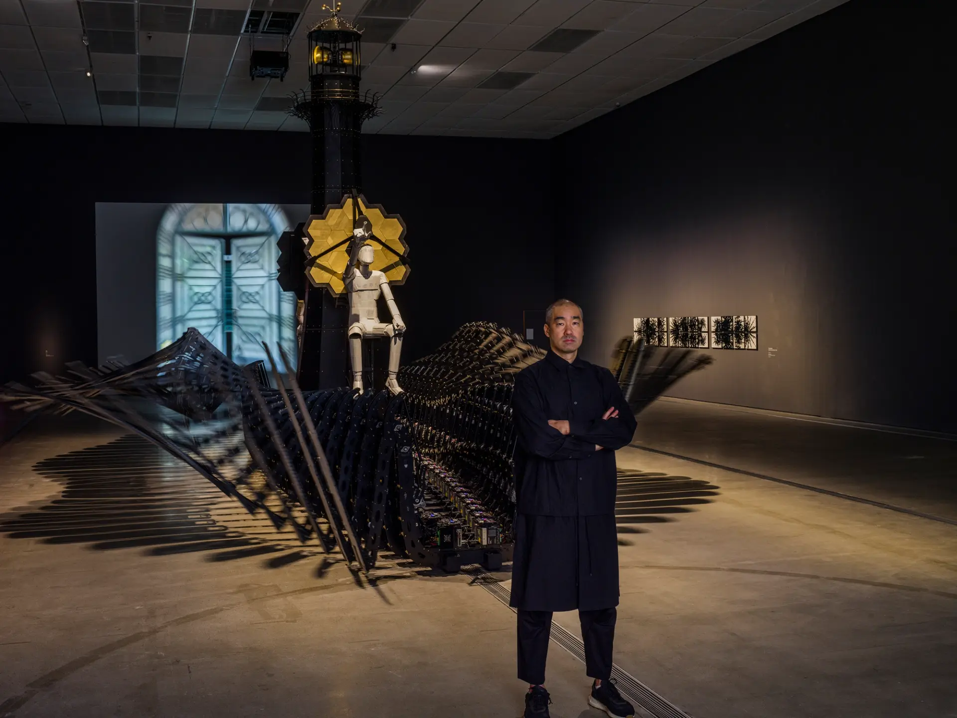 A person observes an intricate installation, topped by a human figure and featuring yellow hexagons.
