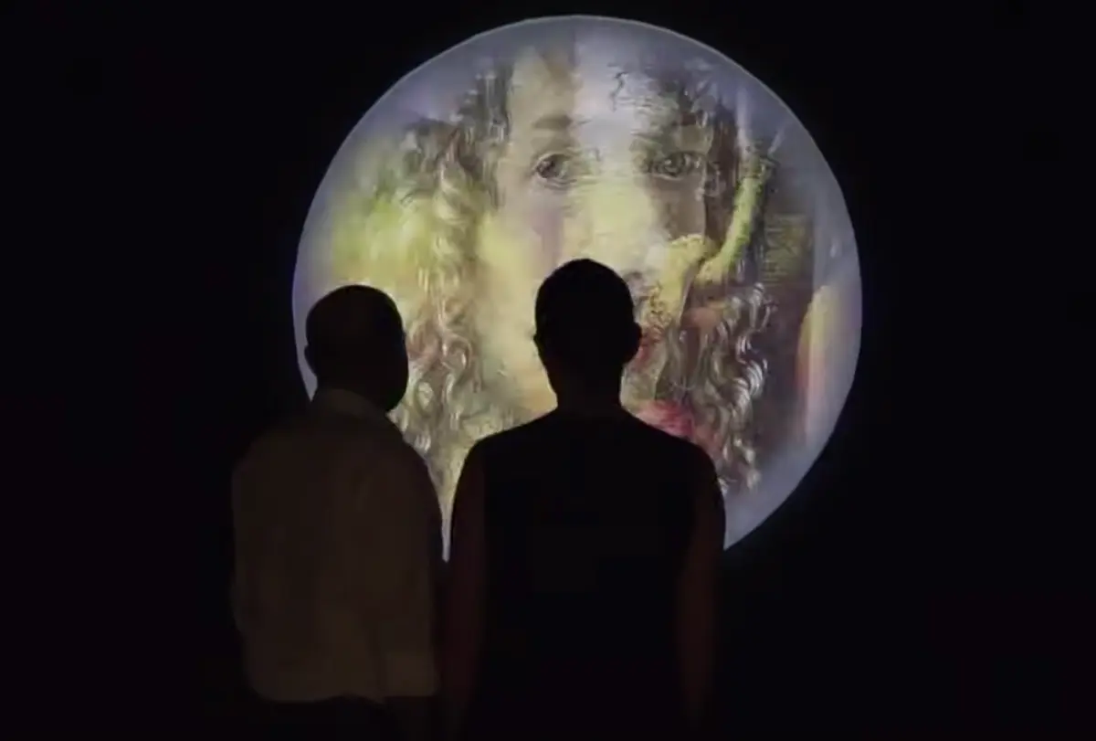 Two individuals are seen from behind, gazing at a projection of an old painted portrait with long curly hair, displayed on a large moon against a black background.