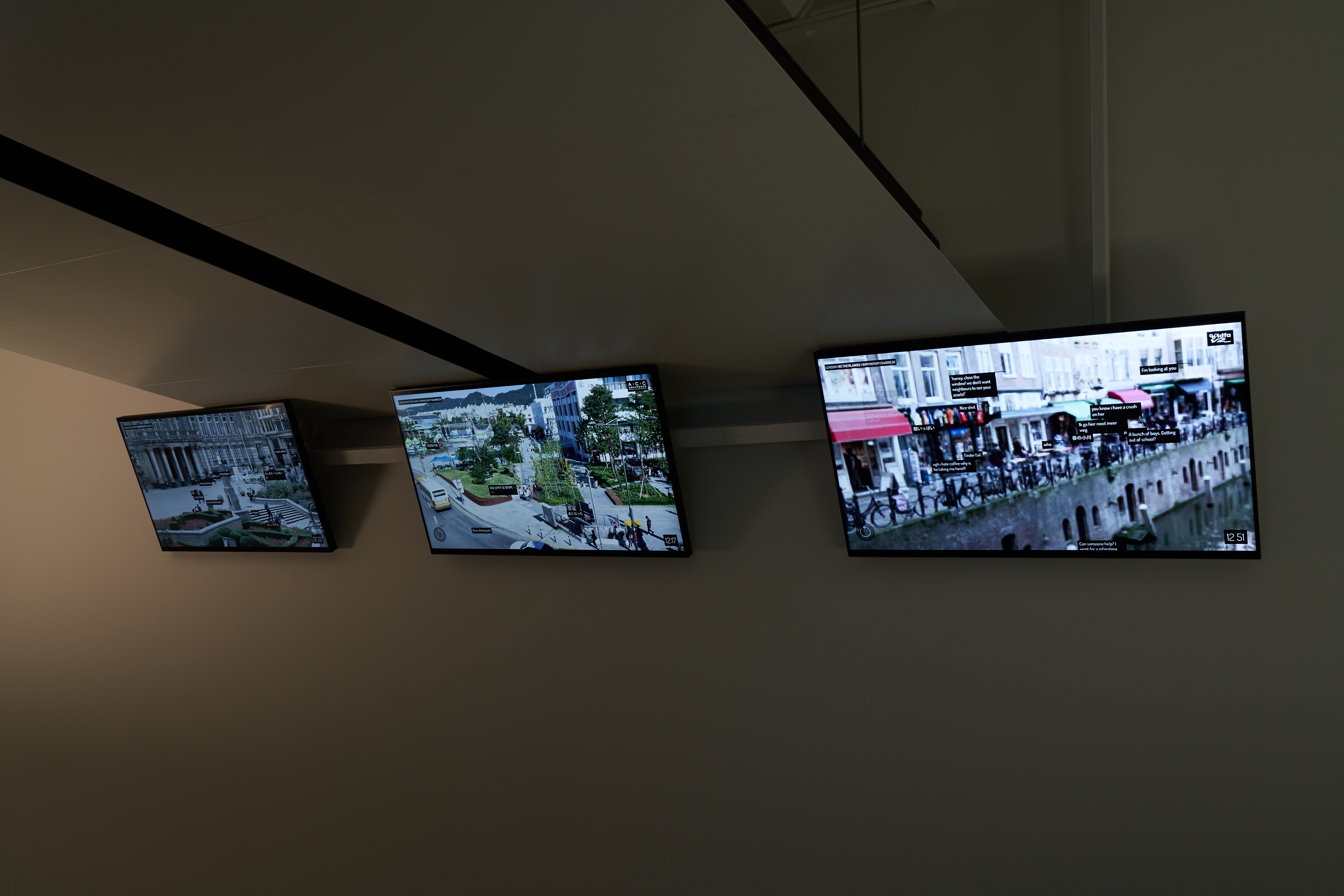 Screens mounted on a ceiling corner showing busy street scenes.