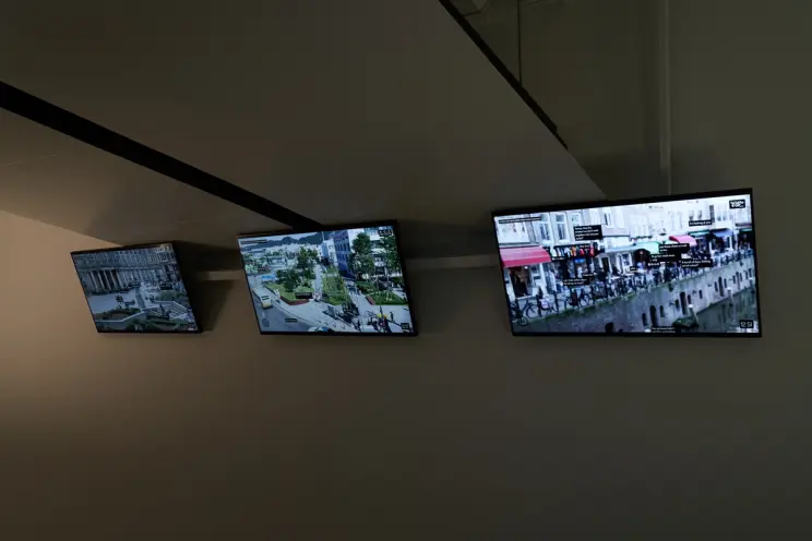 Screens mounted on a ceiling corner showing busy street scenes.