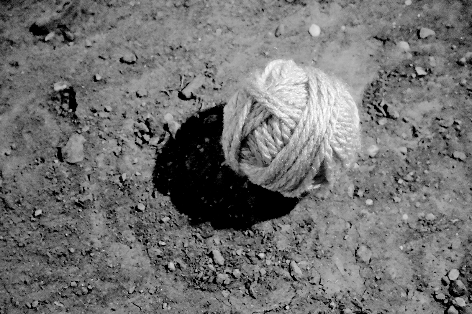 A monochromatic photograph portrays a sizable ball of rope placed on a bare floor, conveying simplicity and minimalism.