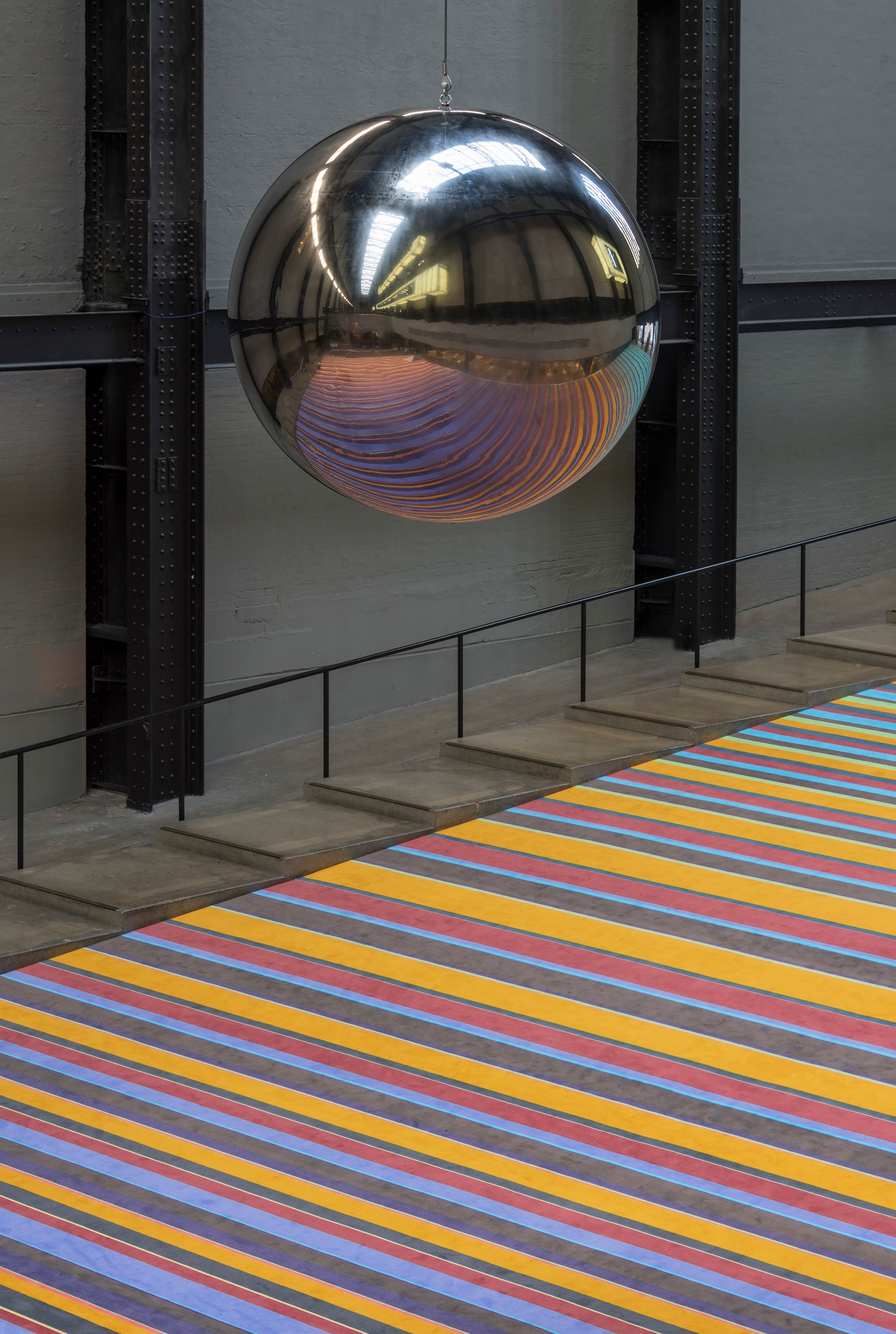 A large sphere hangs above a floor featuring a design of multicolored lines.