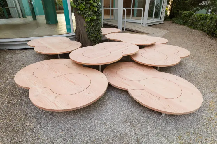 Close-up of wooden tables on gravel, arranged in a cluster with natural wood grain patterns.