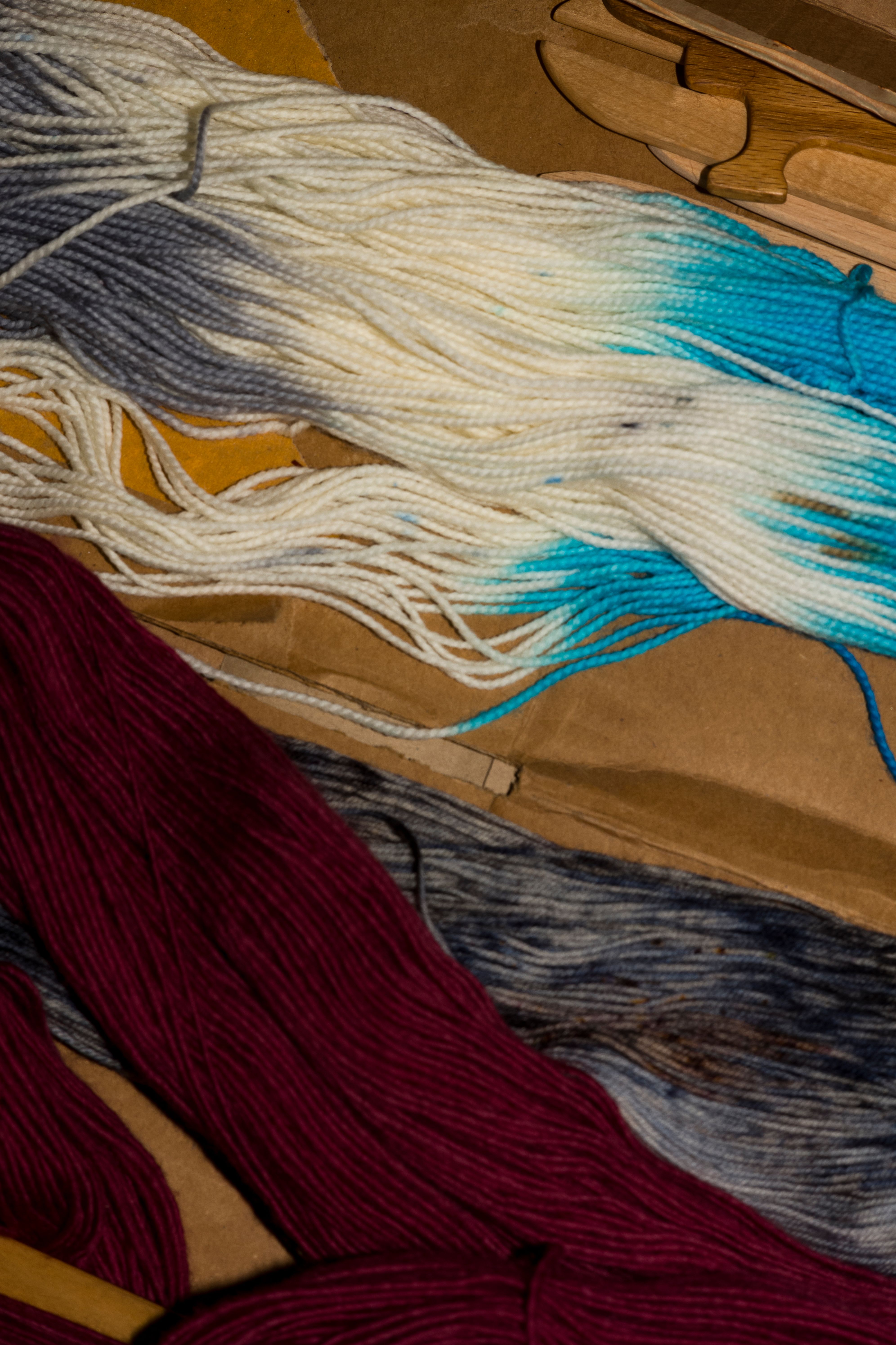 Various colored yarns, including white, turquoise, and maroon, placed on a wooden surface.