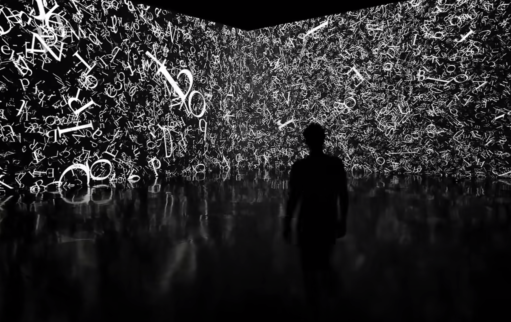 A silhouette of a person stands in a dimly lit room, facing a long, black room divider filled with white letters styled in...