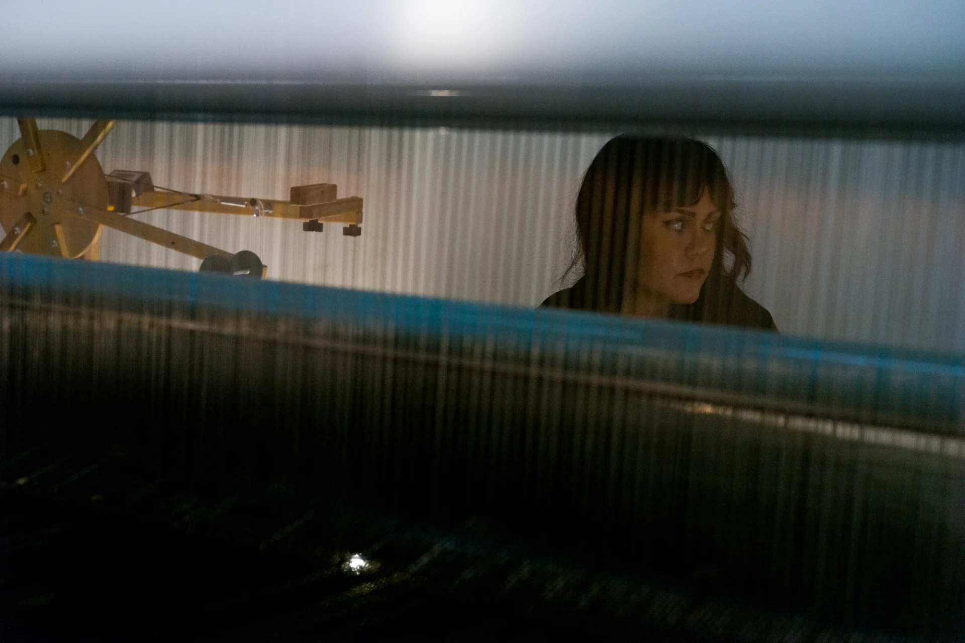 A person viewed through the threads of a loom, focusing intently on their work.