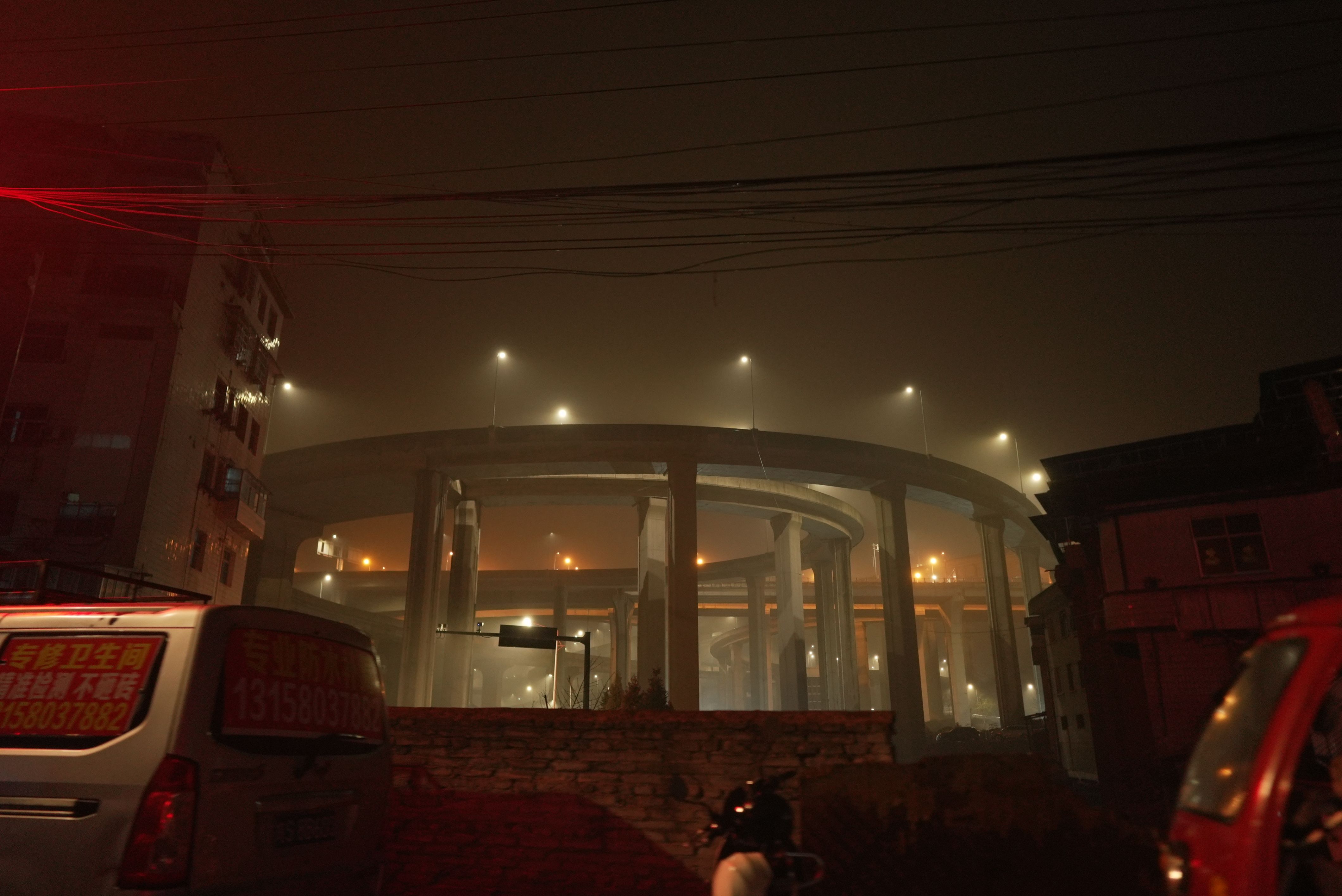 A nighttime shot of a large, cylindrical infrastructure standing tall near a building. The scene is illuminated by several...