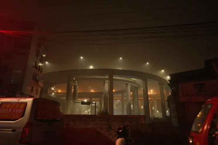 A nighttime shot of a large, cylindrical infrastructure standing tall near a building. The scene is illuminated by several...
