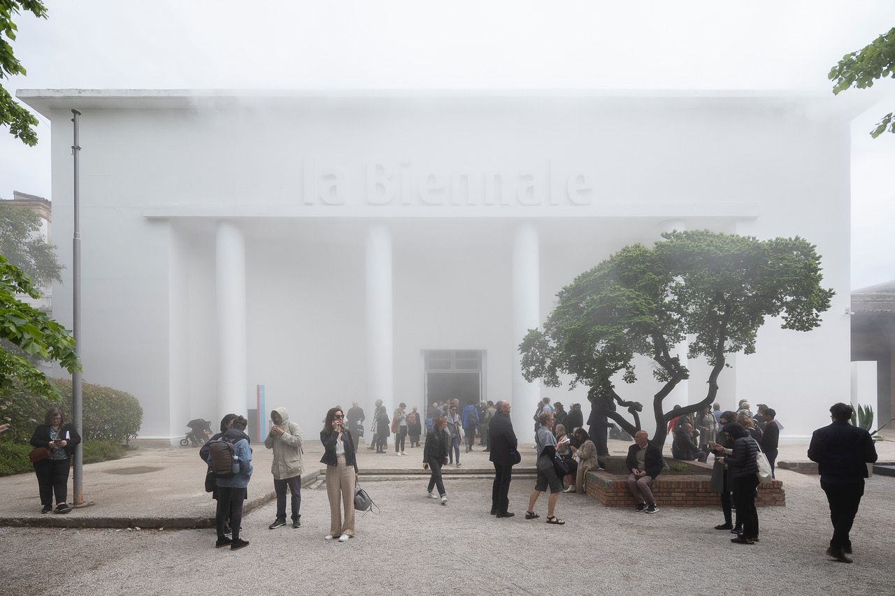 A bustling courtyard filled by a crowd of people in front of a grand white building, accentuated with architectural pillars.