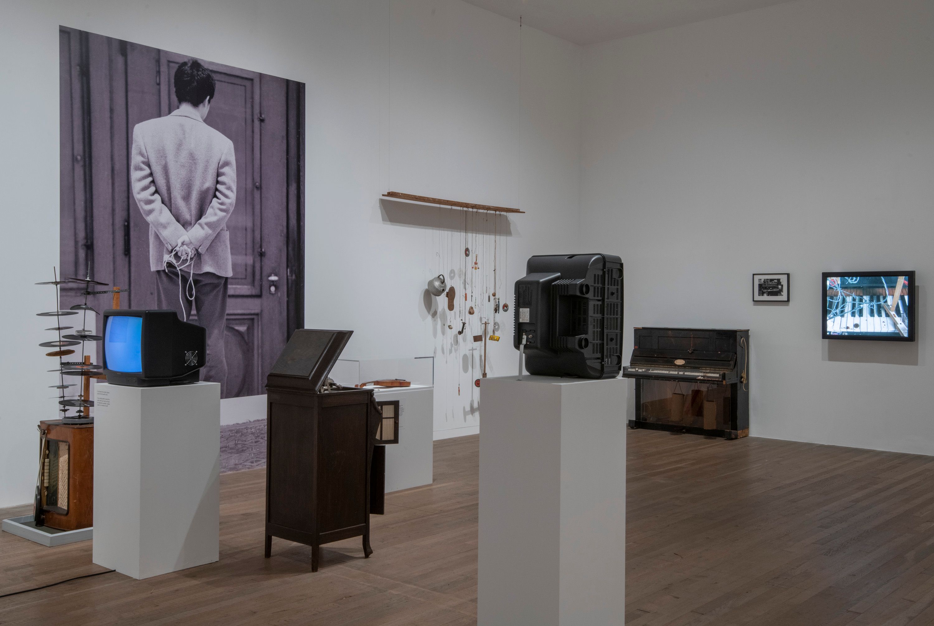 An image displaying a gallery with pristine white walls and polished wooden floors. Wall-mounted televisions and varied ar...