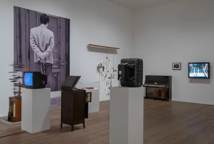An image displaying a gallery with pristine white walls and polished wooden floors. Wall-mounted televisions and varied ar...