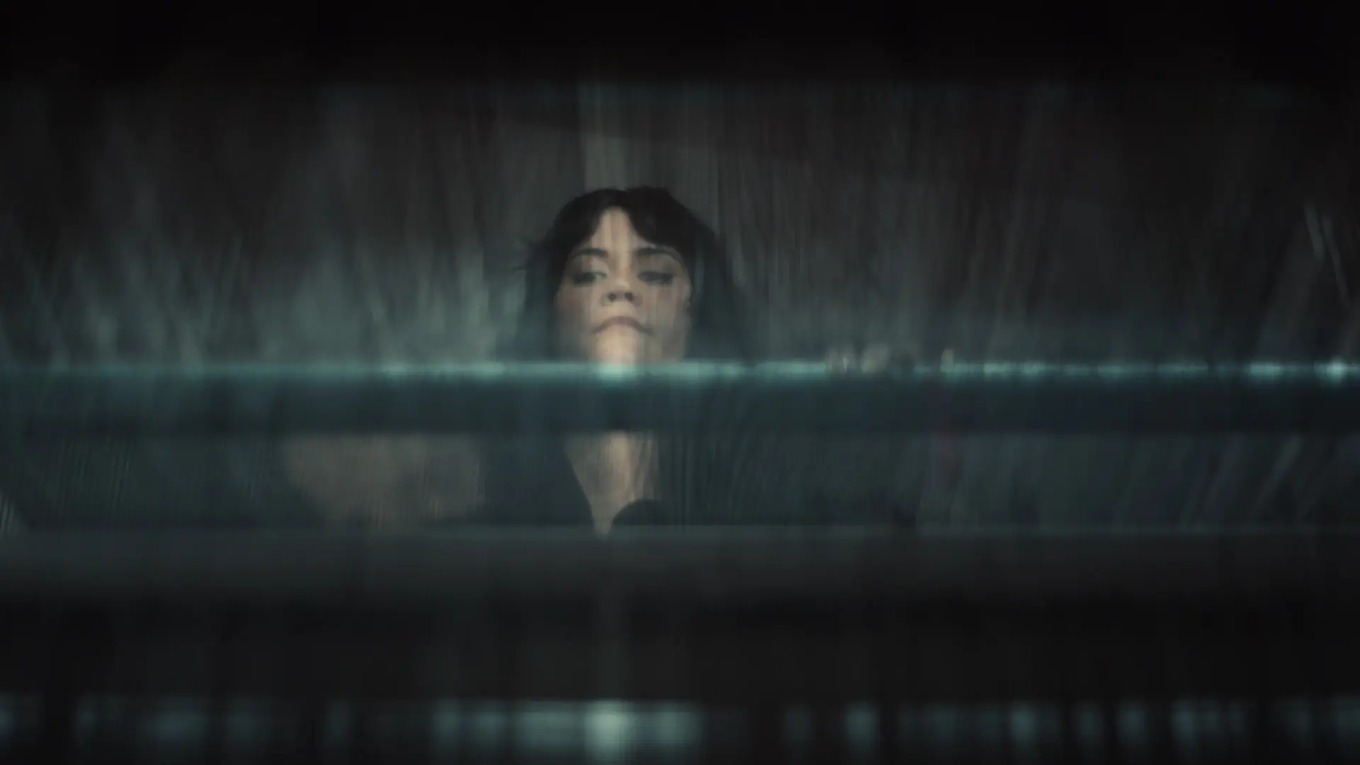 A person looks up through blurred glass or fabric, with blue and gray hues creating a mysterious, atmospheric effect.