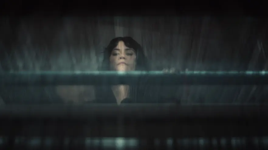 A person looks up through blurred glass or fabric, with blue and gray hues creating a mysterious, atmospheric effect.