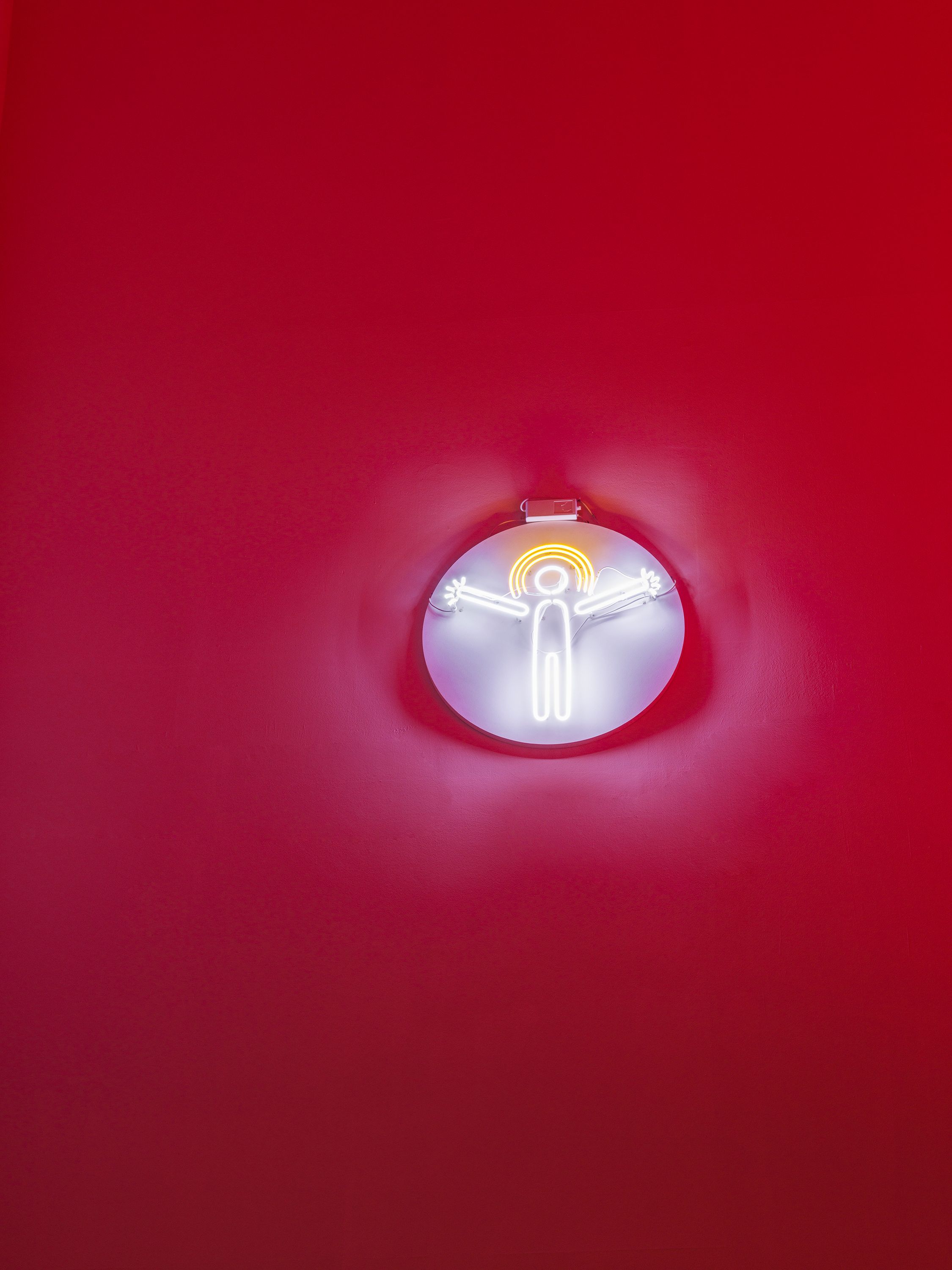 A neon sign featuring a radiant human form encapsulated within a circular shape, mounted on a vibrant red surface.