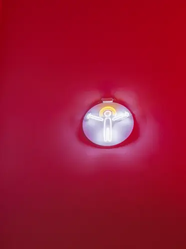 A neon sign featuring a radiant human form encapsulated within a circular shape, mounted on a vibrant red surface.
