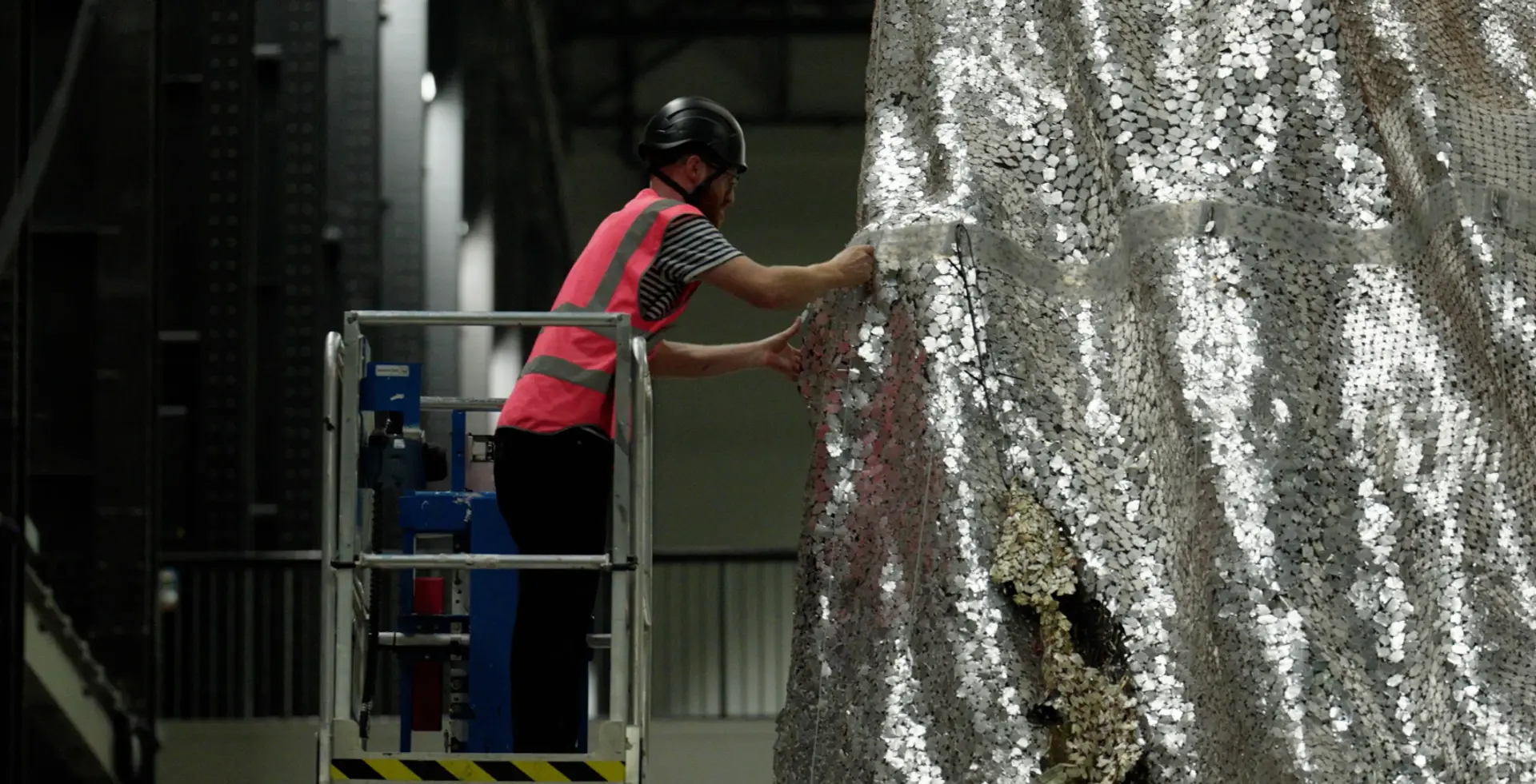 A person on a cherry lift handling a hanging sculpture.