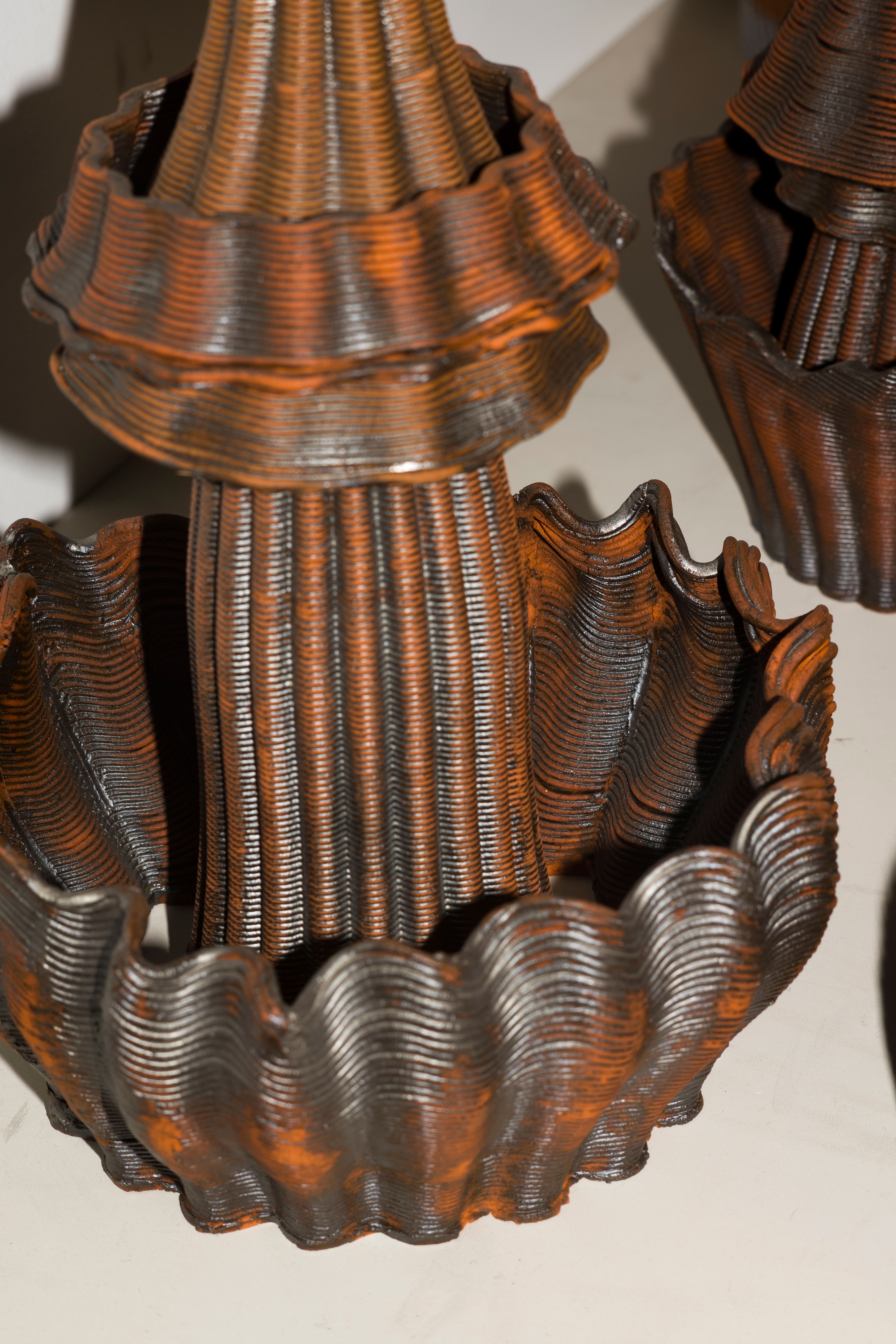 Bronze-colored sculptural forms with ridged and flowing shapes arranged on a flat surface.