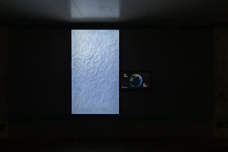 A video art installation showing a large ocean wave with a small Earth image.