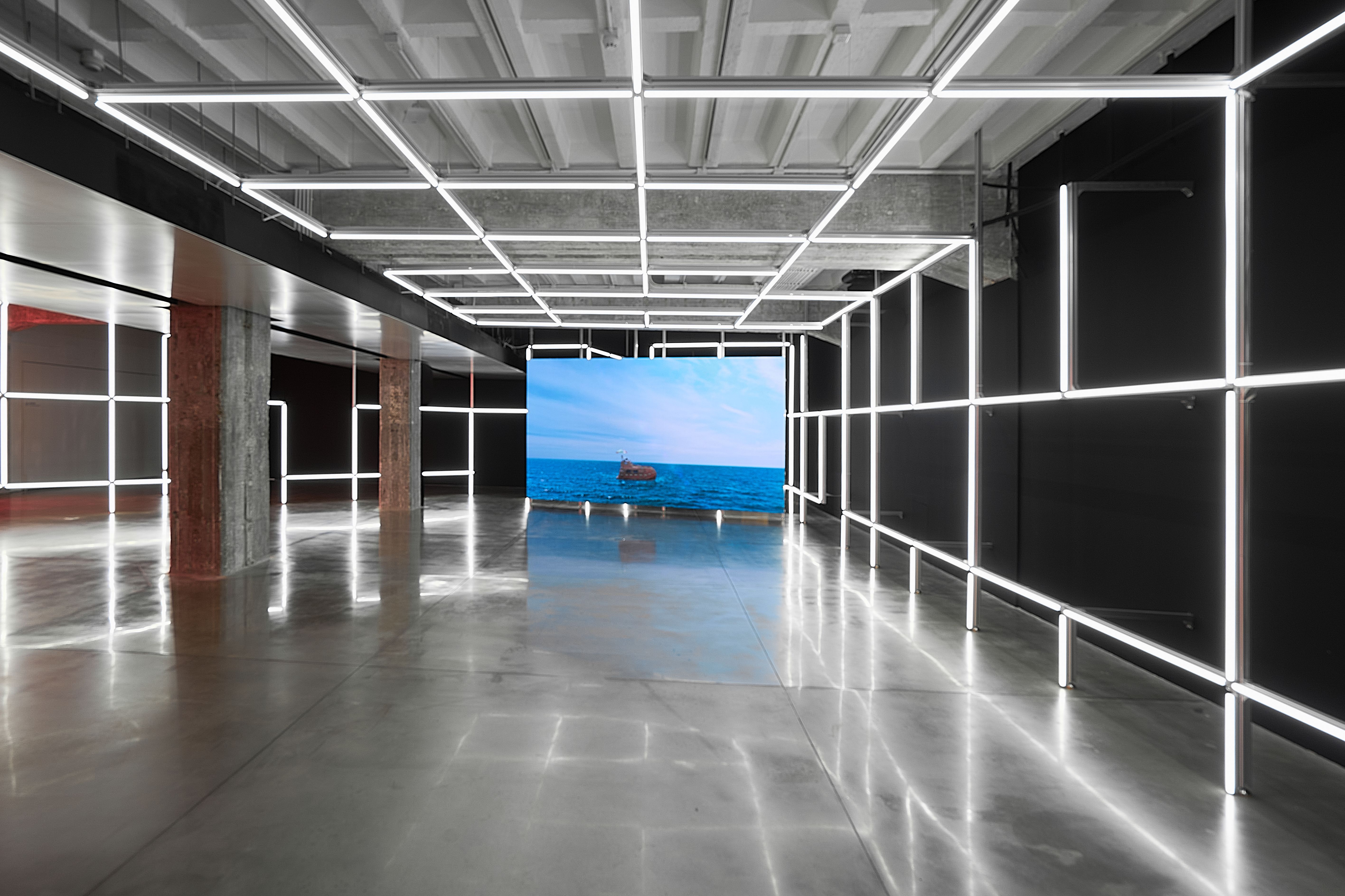 A minimalist installation fa large screen displaying an ocean scene at the end of the room, creating a serene and futurist...