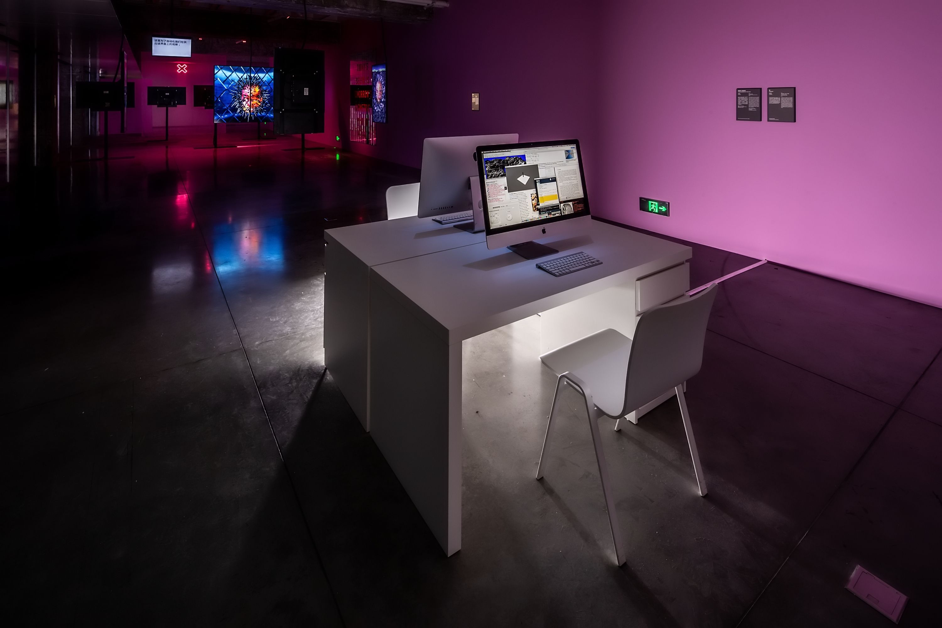 Workspace with a computer inside an art gallery with pink lighting.