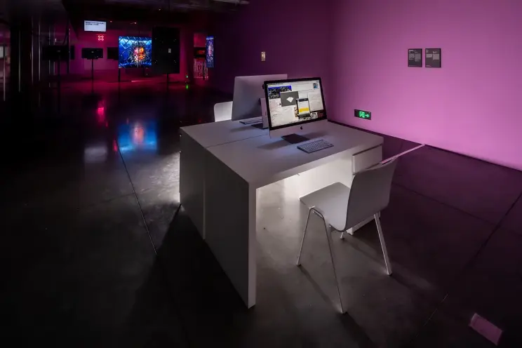 Workspace with a computer inside an art gallery with pink lighting.