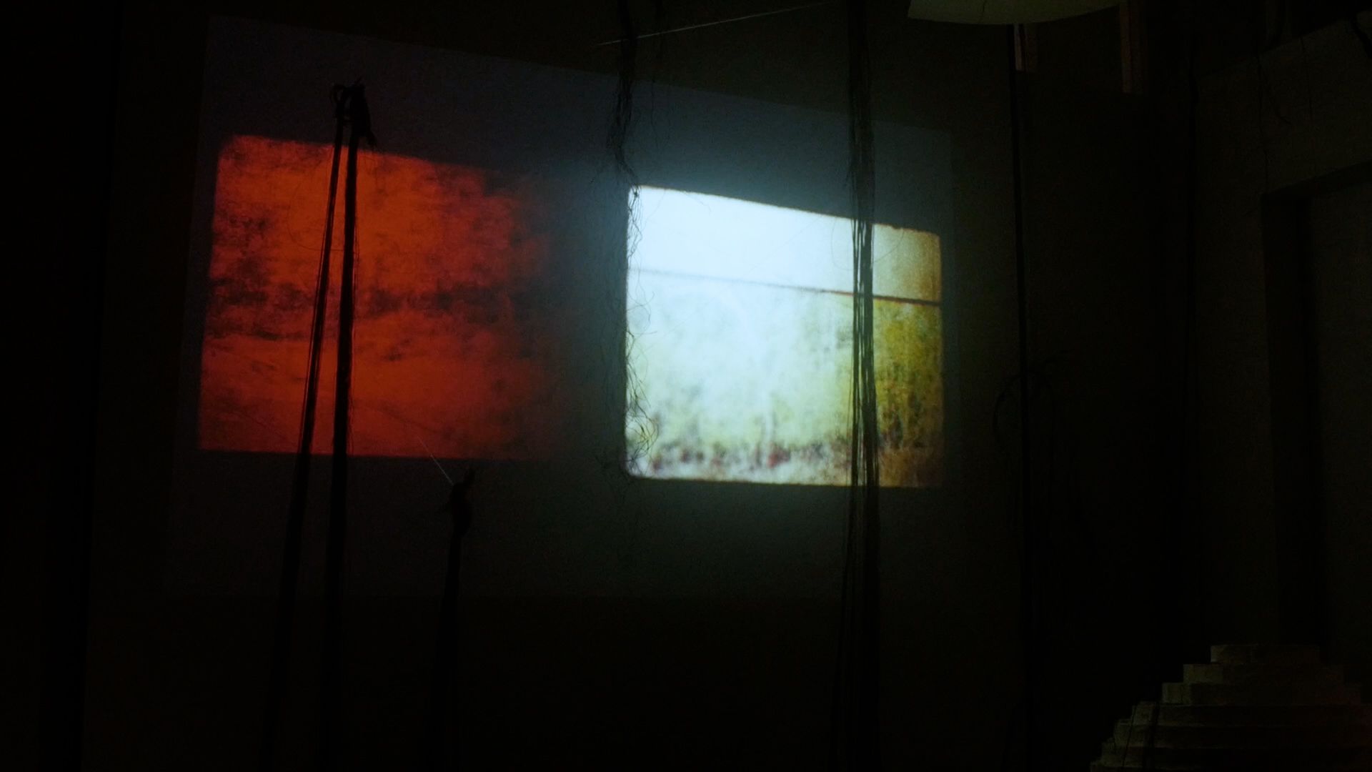 Two adjacent projections, one glowing red and the other pale yellow-green, illuminate a dark installation space.