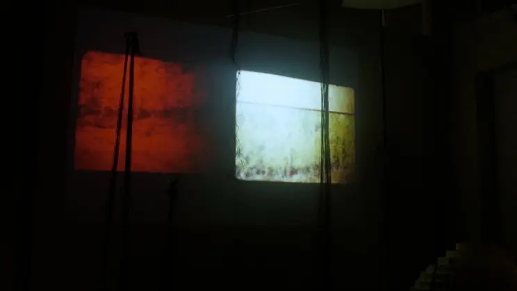 Two adjacent projections, one glowing red and the other pale yellow-green, illuminate a dark installation space.