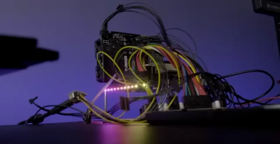 A dimly lit room housing a table cluttered with an assembly of various electronics, lights, and wire.