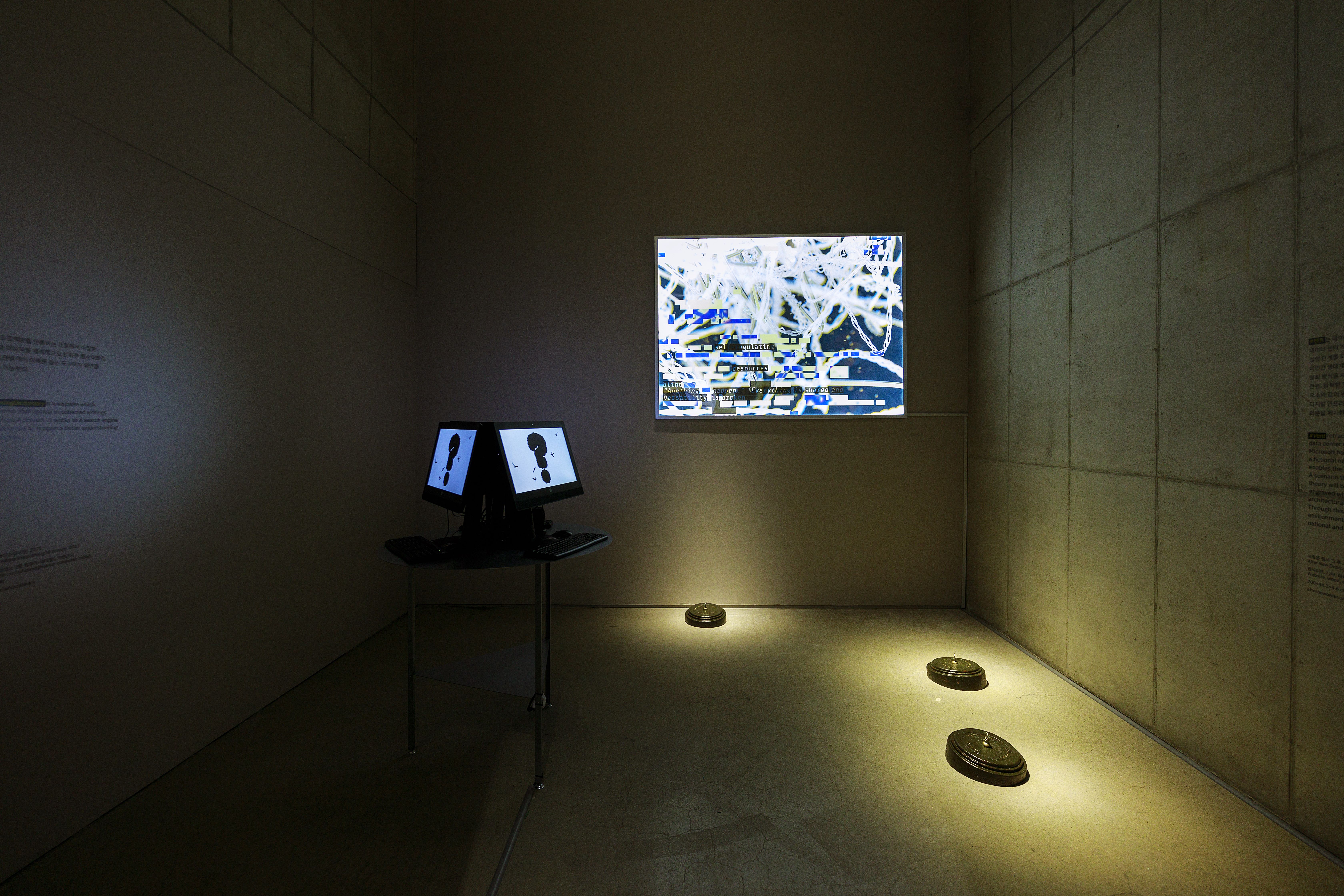 Several rounded, illuminated objects are positioned on the floor of a dimly-lit room, surrounded by various display screen...