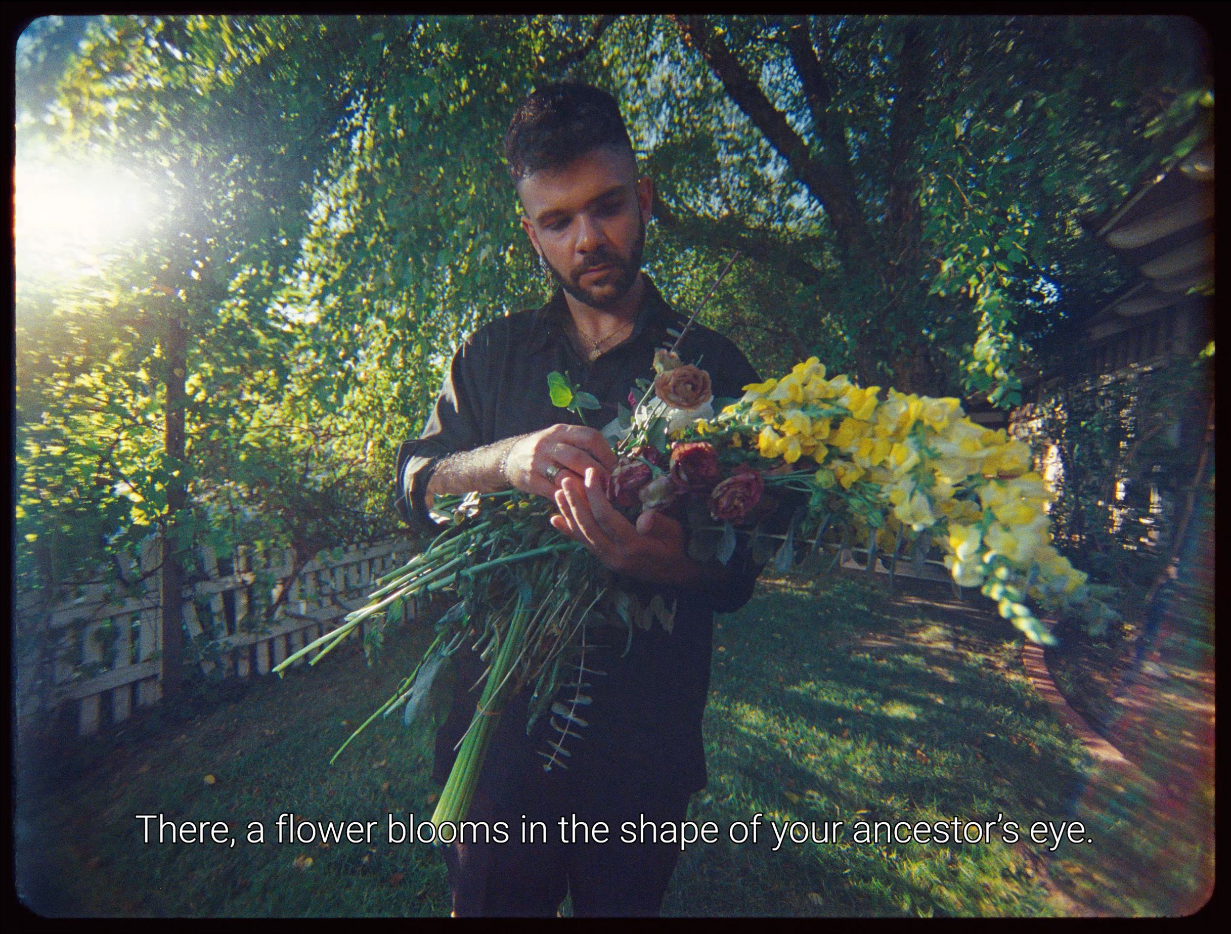 A man holding a large bouquet of flowers in a sunlit garden with the caption, "There, a flower blooms in the shape of your ancestor’s eye."