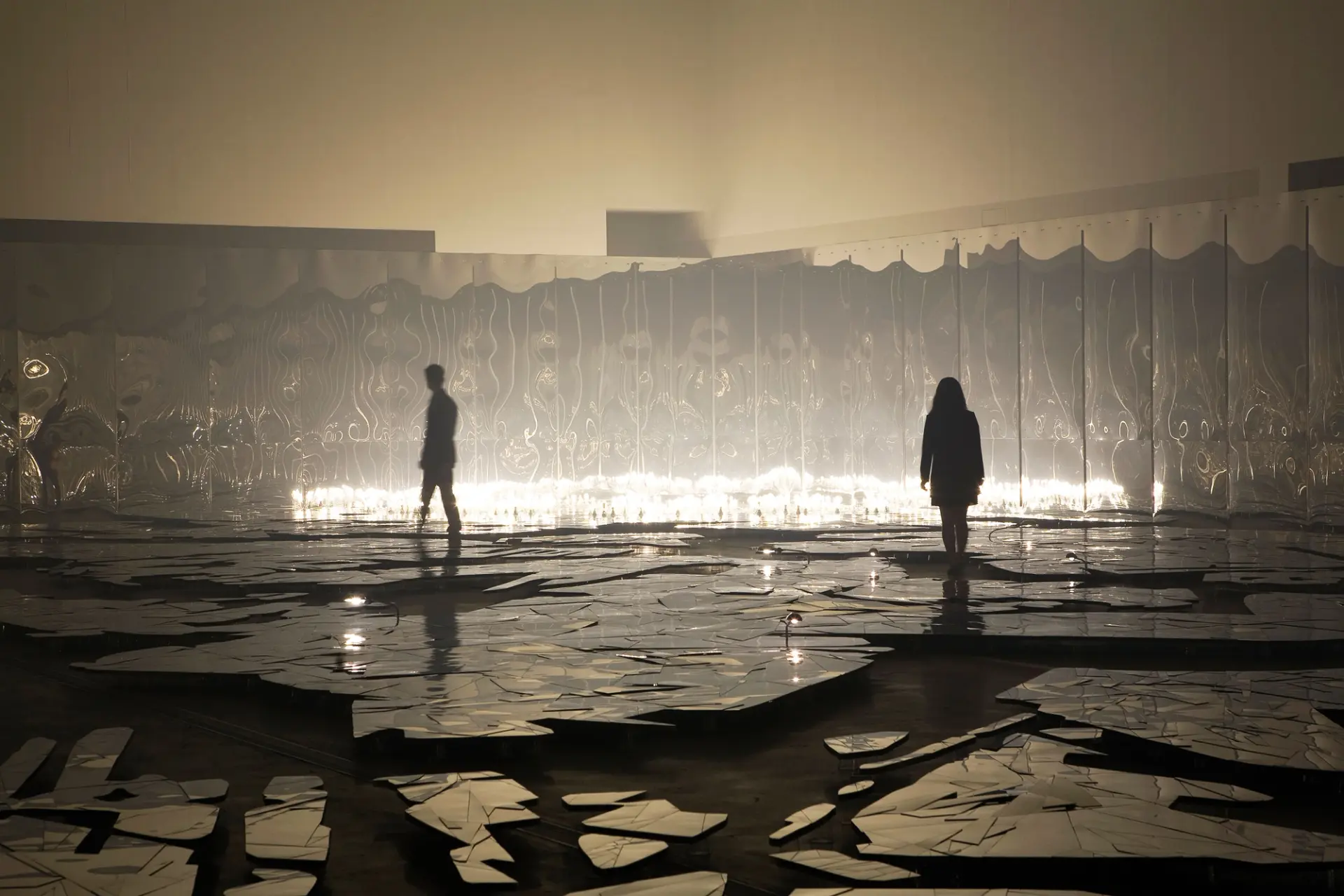 Curvy mirror walls reflect the dark showroom floor, where people are walking on a surface made to look like broken glass, ...