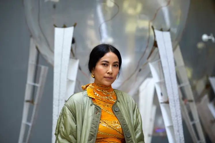 An artist stands before their large-scale art installation, observing the intricate details.