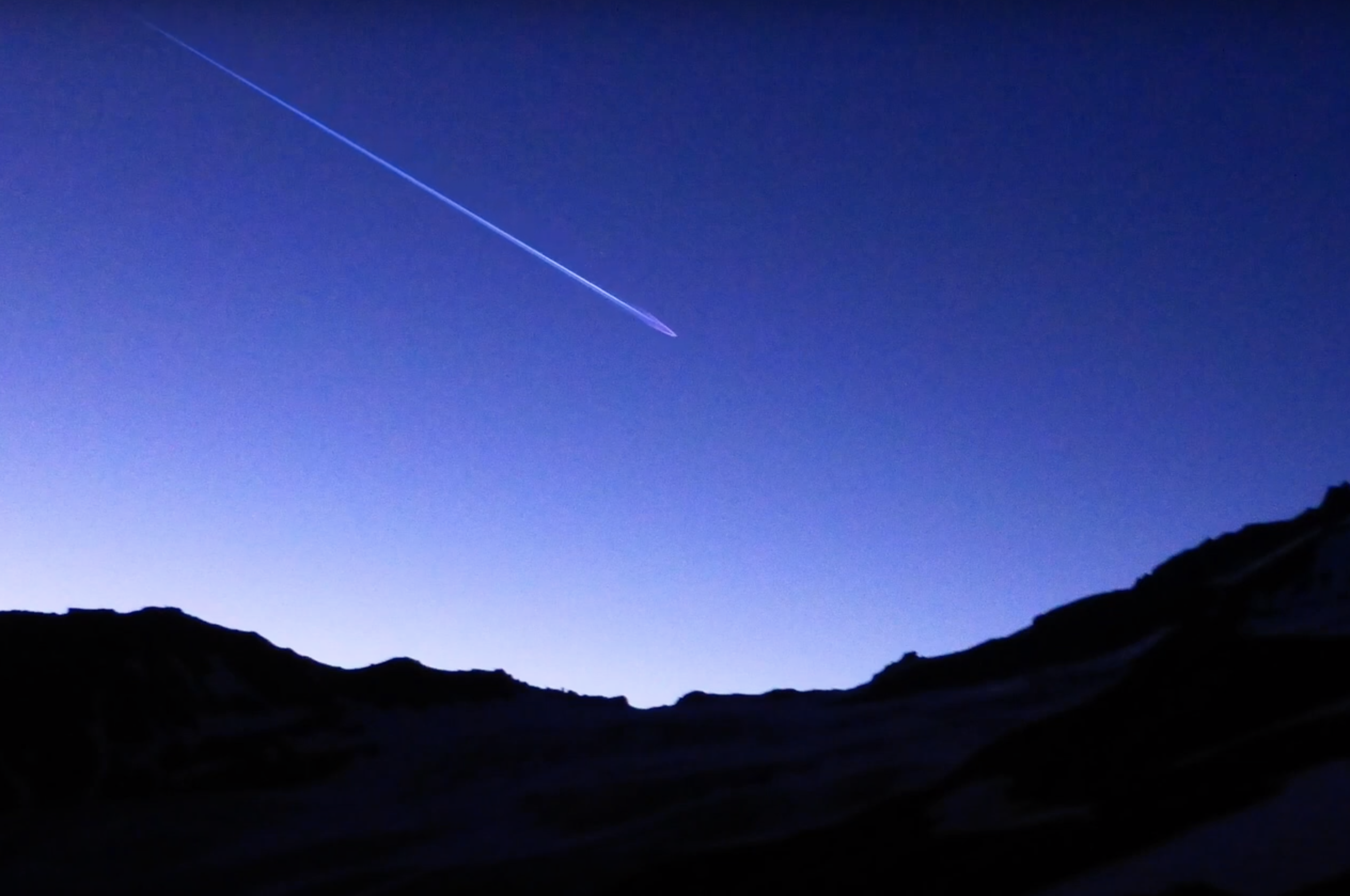A vivid, atmospheric landscape under a sky streaked with shooting stars. Mountains outline the horizon beneath the electri...