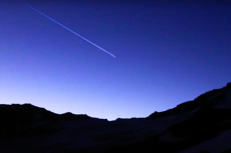 A vivid, atmospheric landscape under a sky streaked with shooting stars. Mountains outline the horizon beneath the electri...