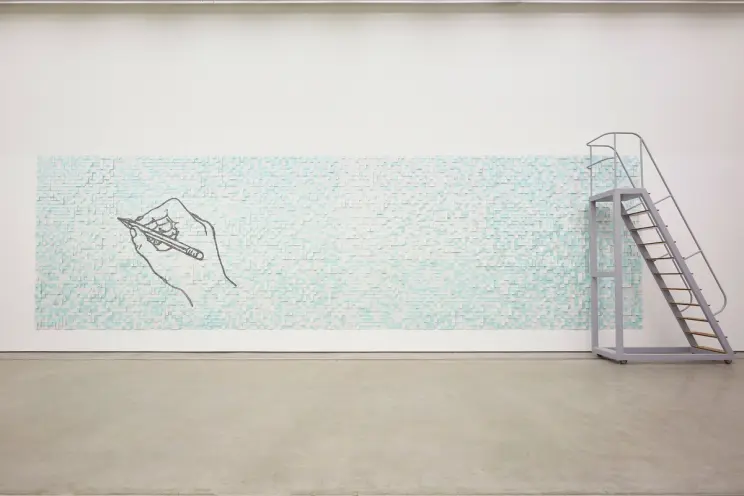 A wide rectangular mosaic art piece in aqua blue, featuring a drawn hand holding a pencil on the left. A silver metal ladd...