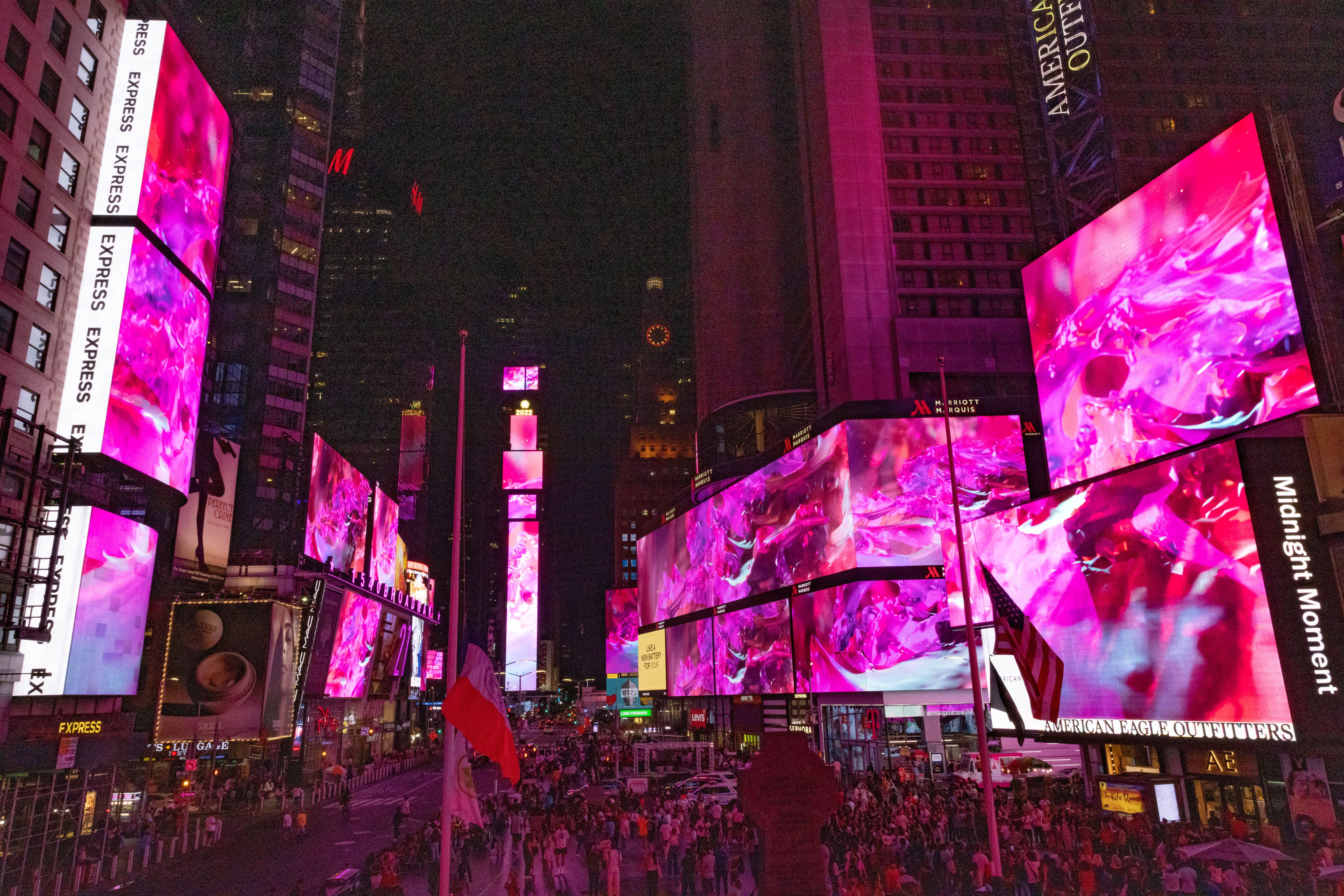 An abstract art installation by Nancy Baker Cahill, titled 'Slipstream', adds a splash of pink hues amidst the advertising screens in Times Square. The surrounding buildings loom in the background.
