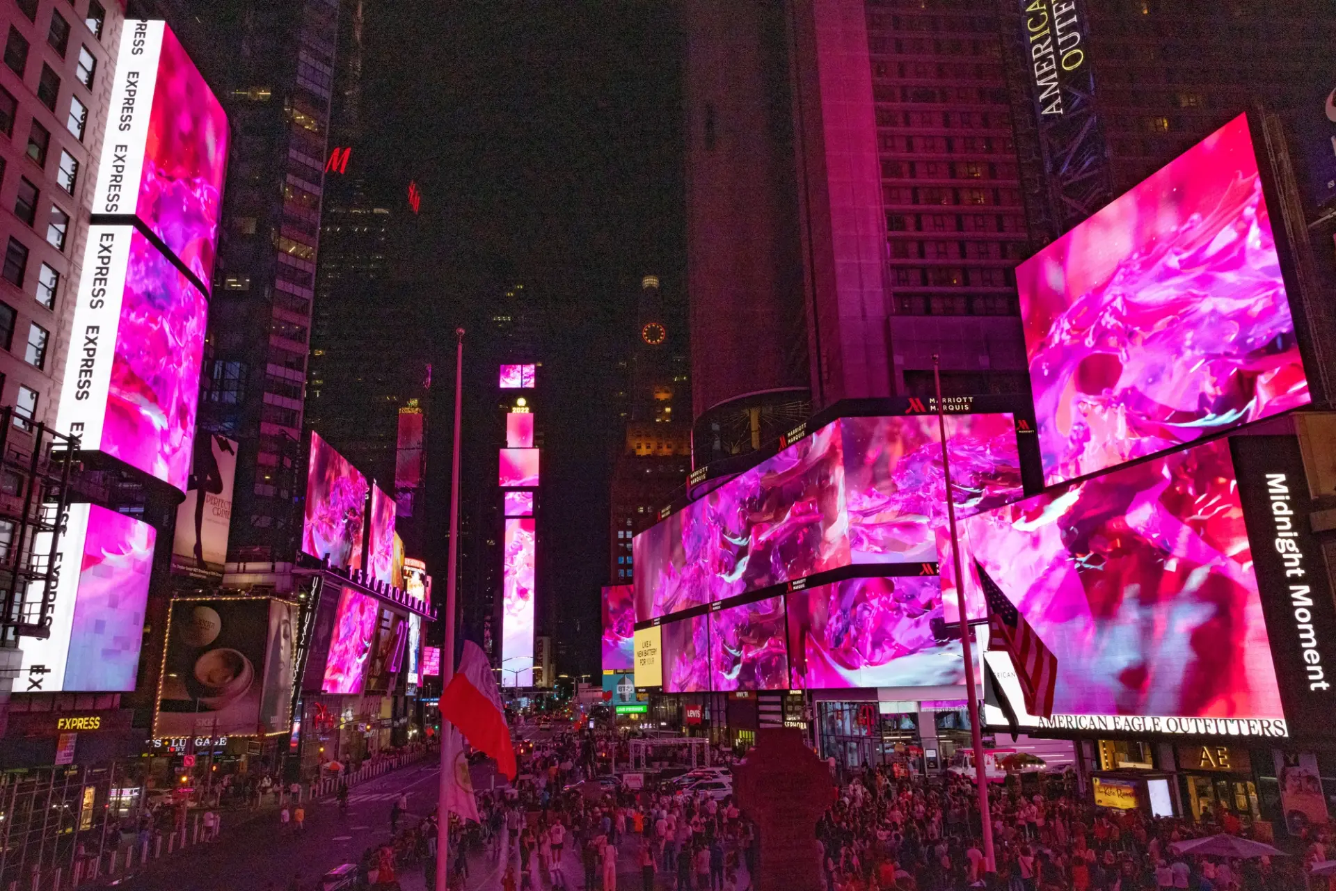 An abstract art installation by Nancy Baker Cahill, titled 'Slipstream', adds a splash of pink hues amidst the advertising screens in Times Square. The surrounding buildings loom in the background.