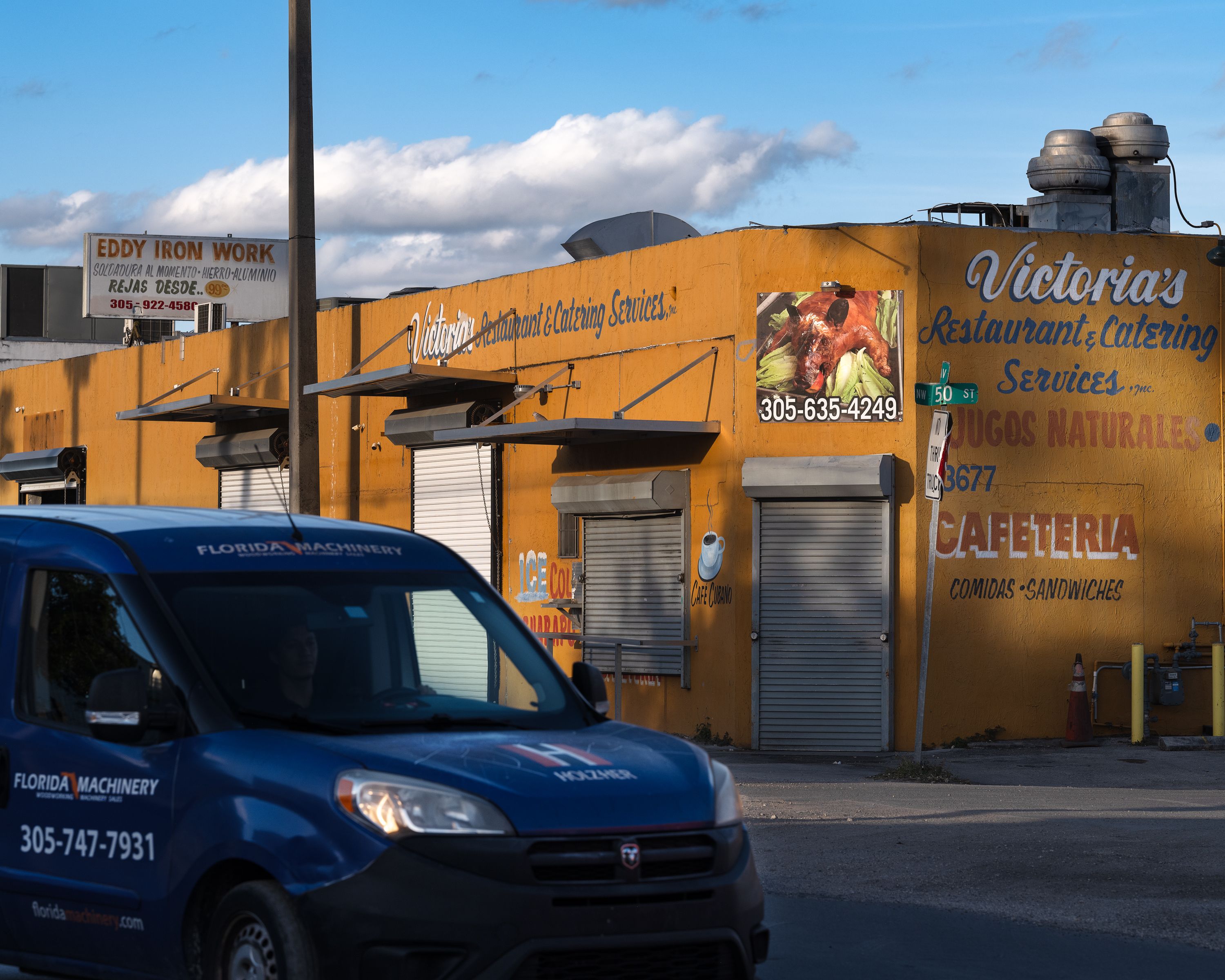 A car parked outside of a restaurant and catering services warehouse.