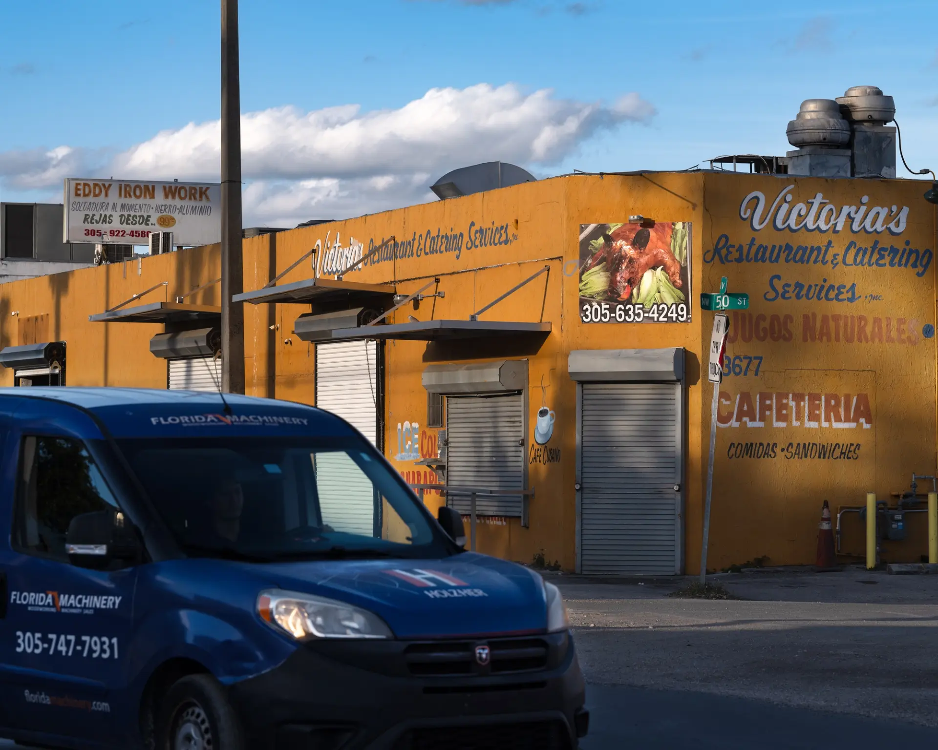 A car parked outside of a restaurant and catering services warehouse.