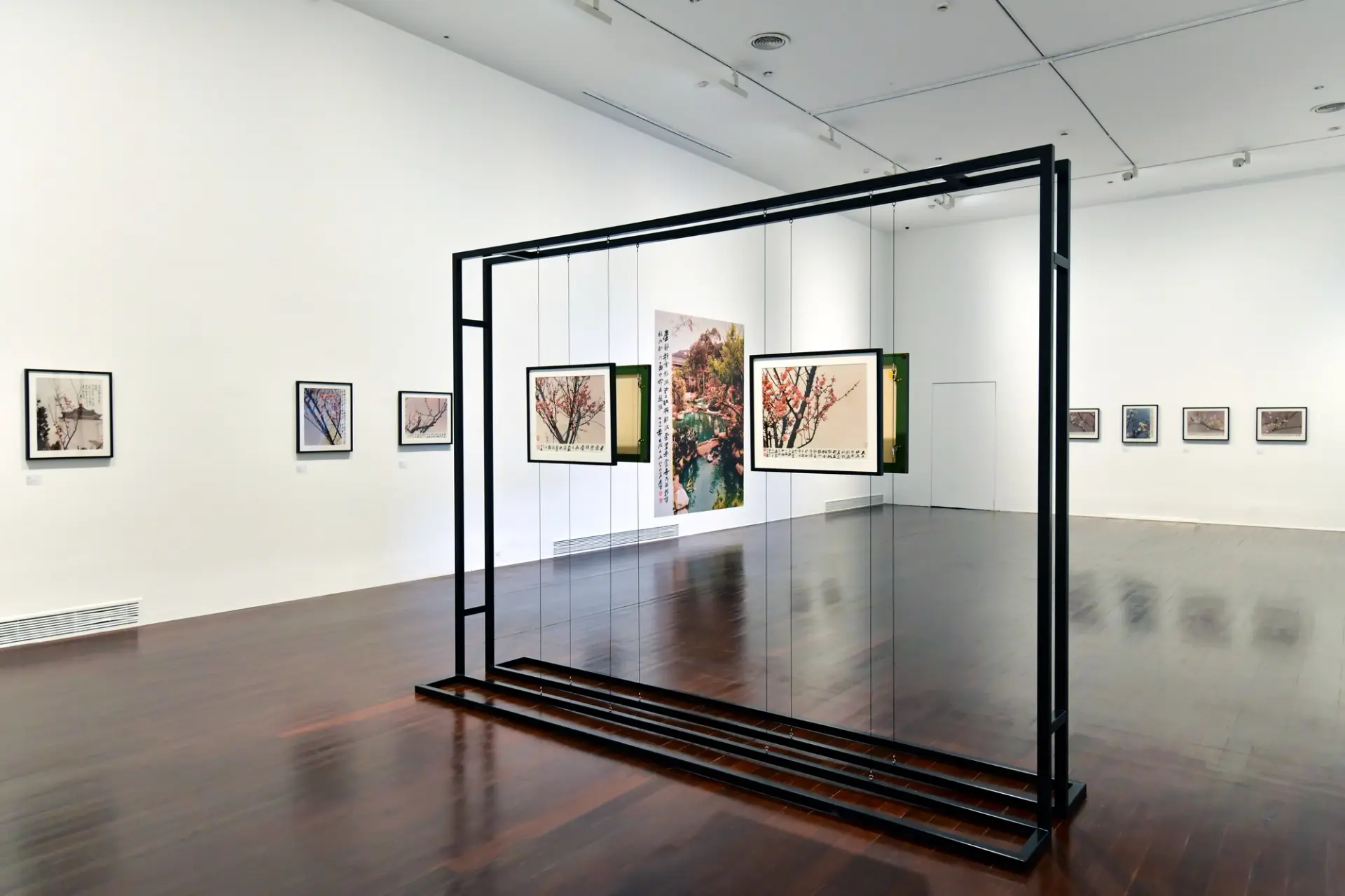 A spacious white gallery room with polished wooden flooring showcases an exhibition of framed photographs depicting Japane...